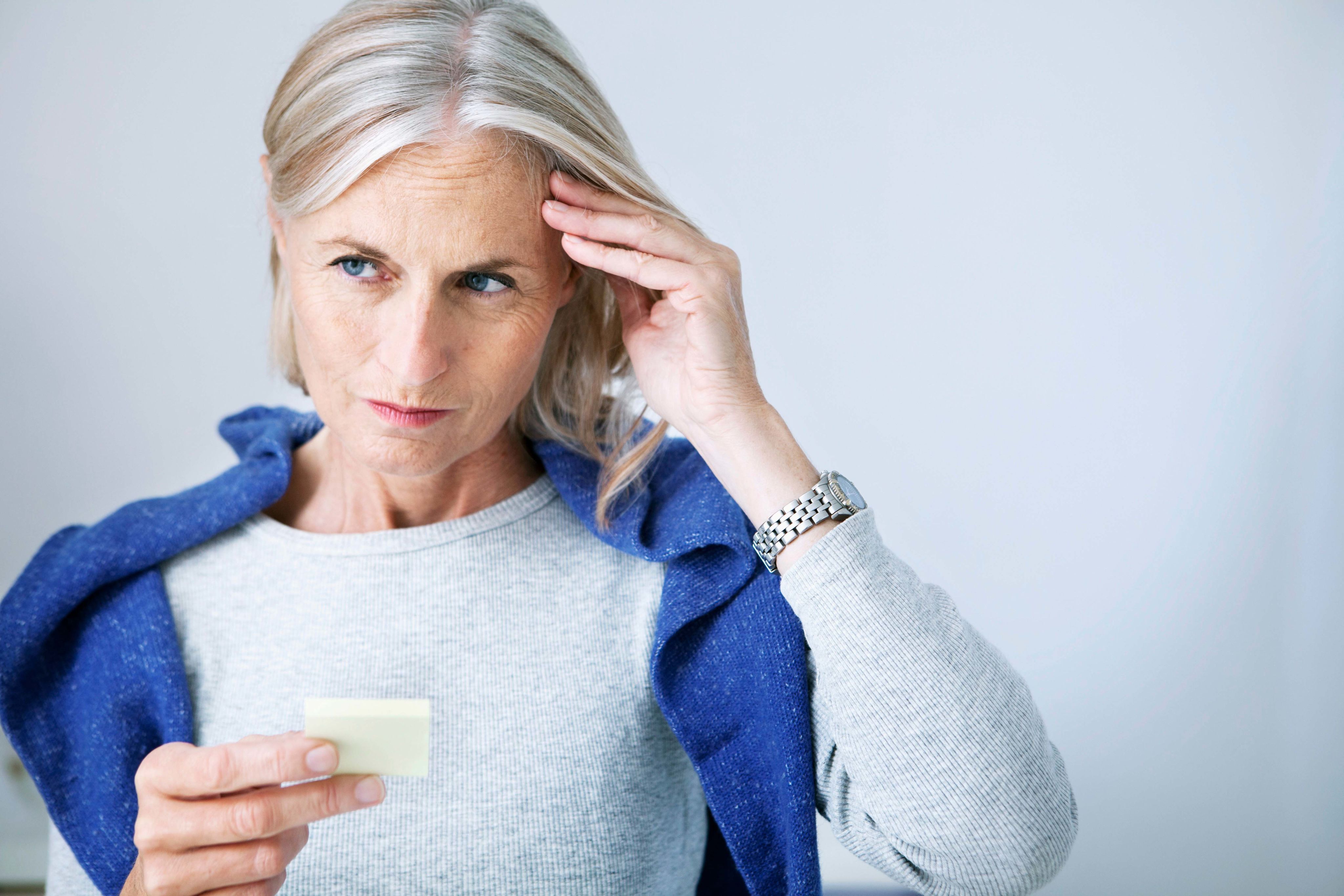 Woman with one hand on her head looking at a post-it.
