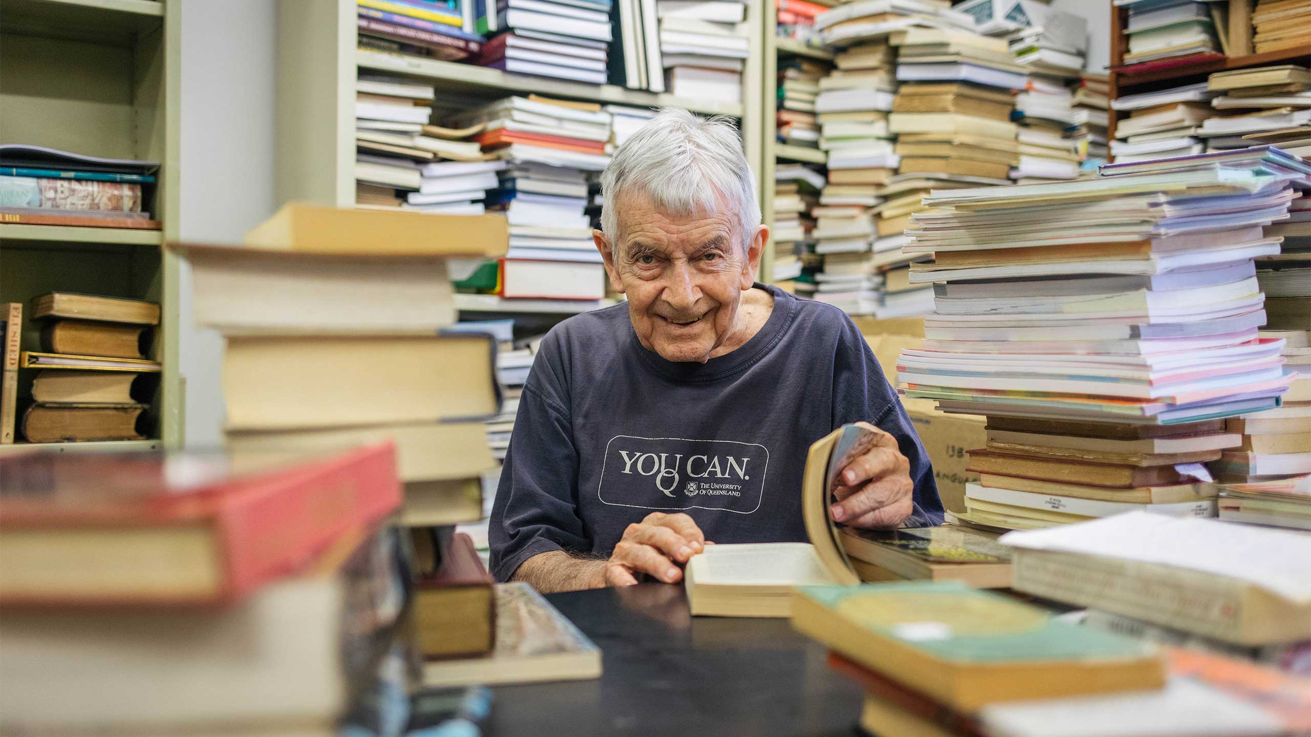 UQ Alumni Book Fair volunteer Donald Barrett AM surrounded by books.