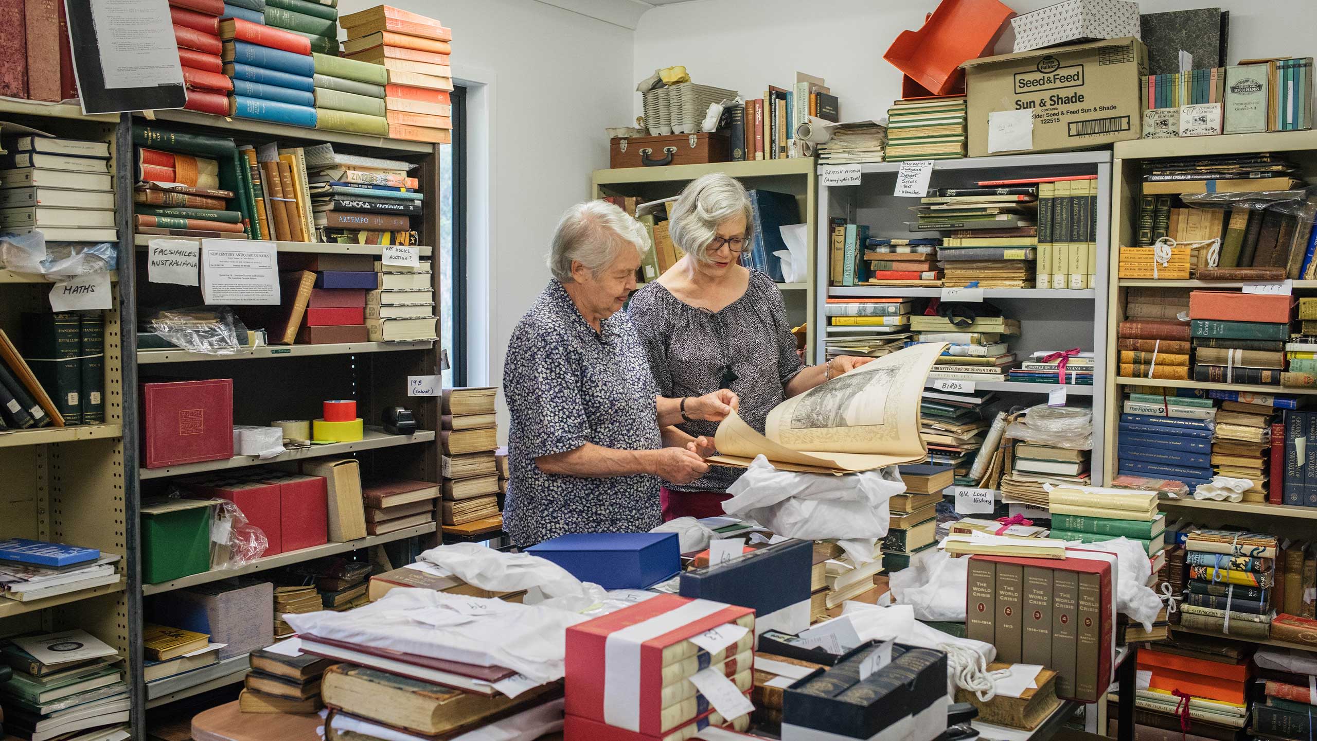 An image of UQ Alumni Book Fair rare book co-convenors Jan Thompson and Anne Mullins surrounded by books.