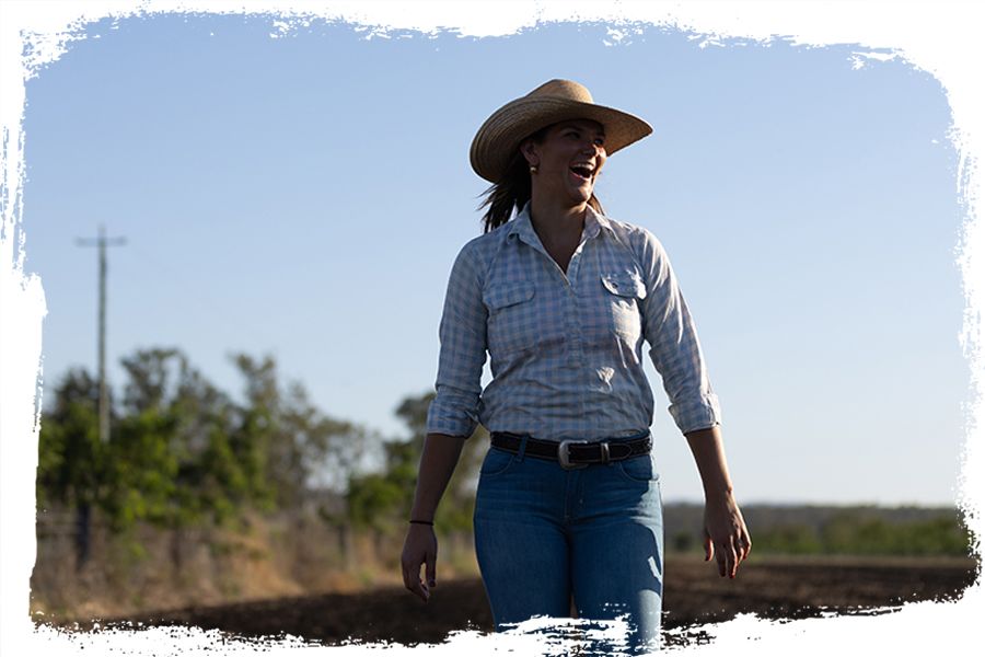 Phoebe Robinson wearing her farming clothes and a hat and laughing at UQ's Gatton campus.