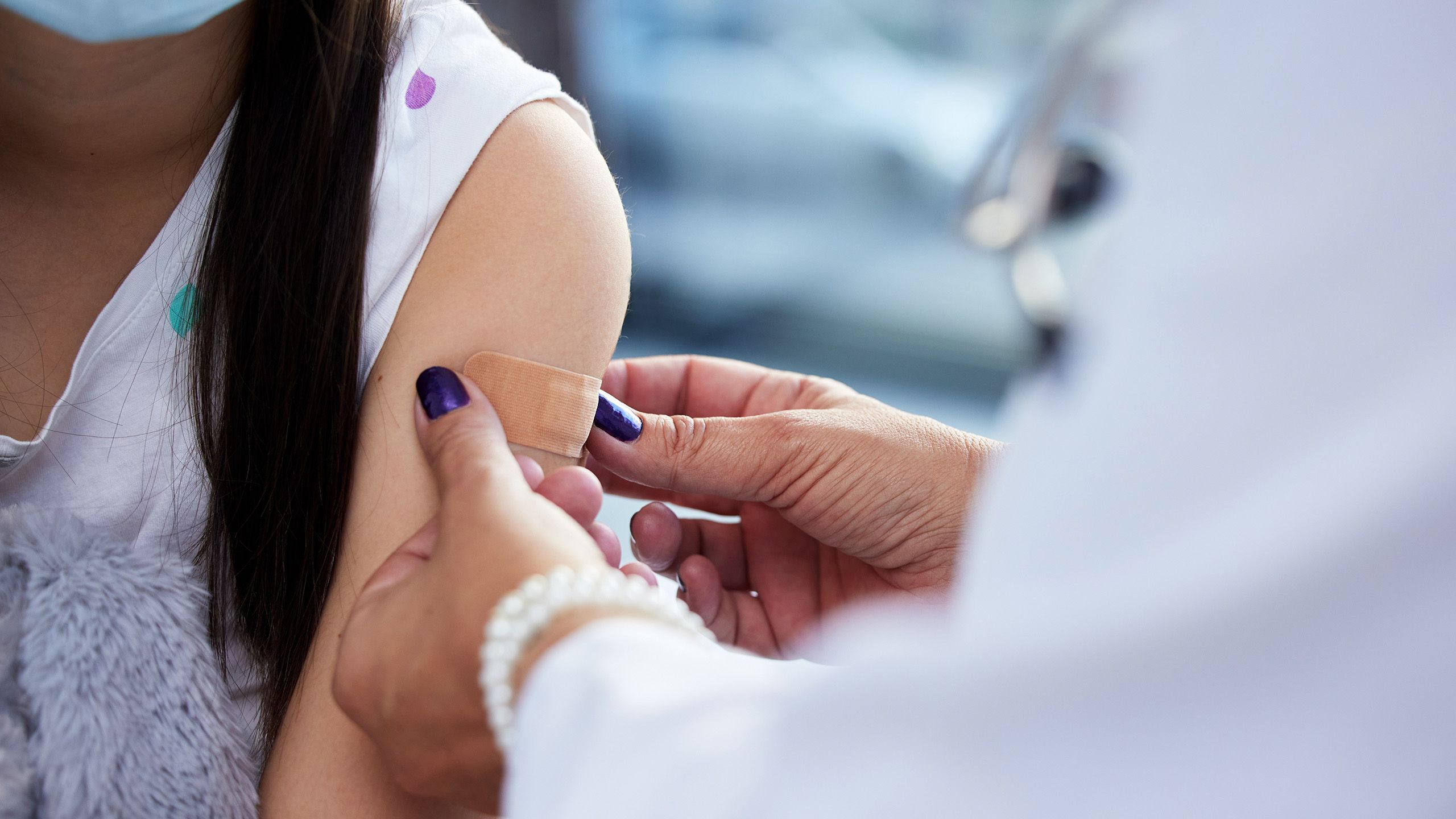 One person sticking a bandaid onto the upper arm of another person