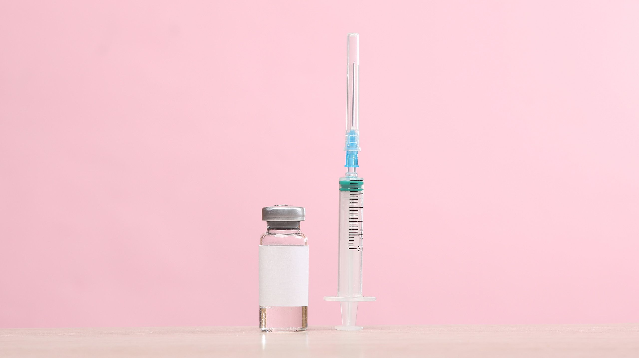 An empty syringe standing up on its base next to a vial of clear liquid