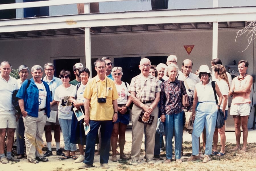 20 people standing on a beach in front of a 2-storey building