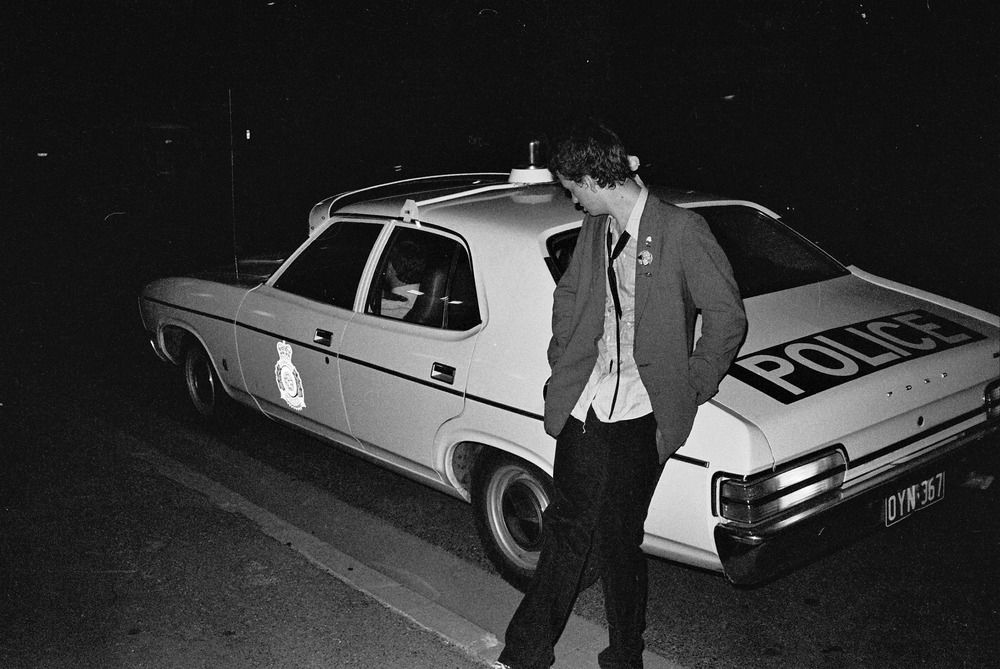 A young man leans against a 1970's Queensland police car.