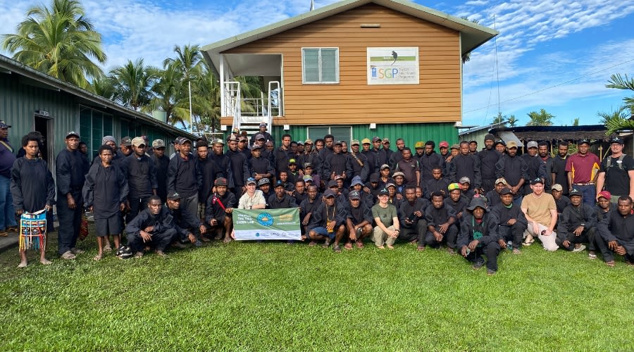 A large group of rangers in navy blue uniforms standing on the grass in front of a wooden house
