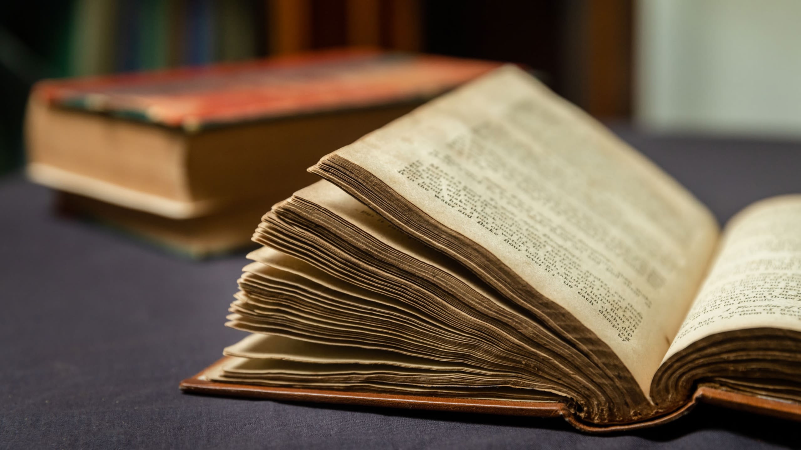 An old browned book laying opened on a table with a blue tablecloth