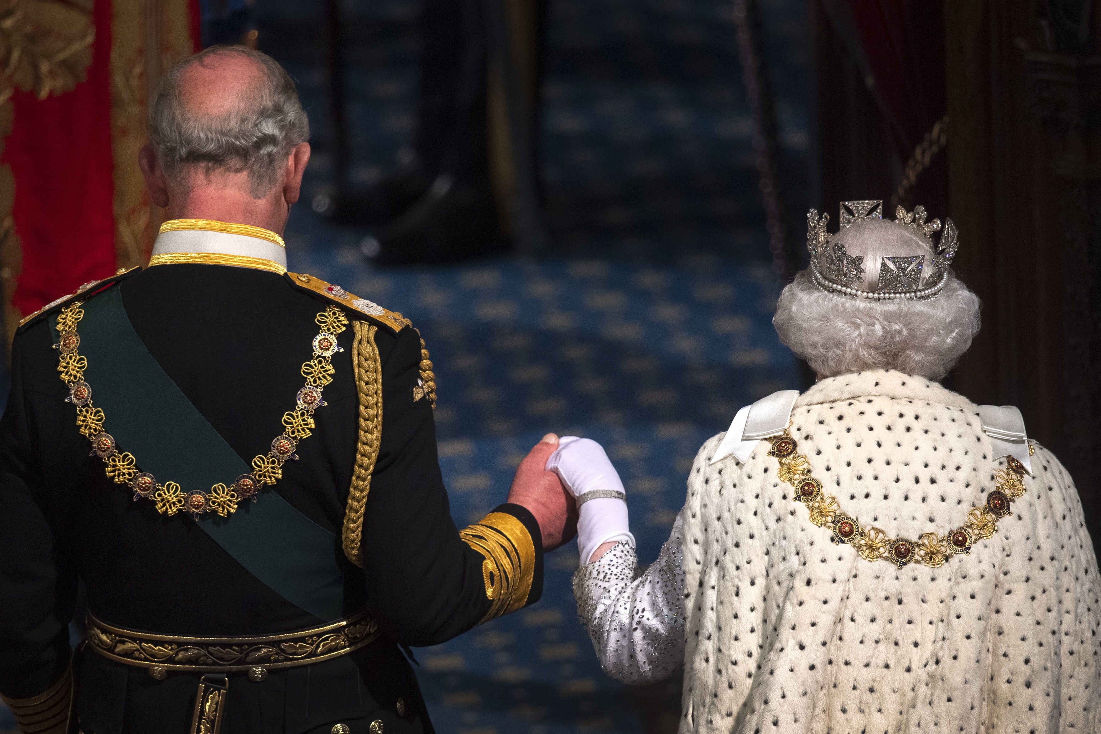 The backs of Prince Philip and Queen Elizabeth as they hold hands walking on blue carpet