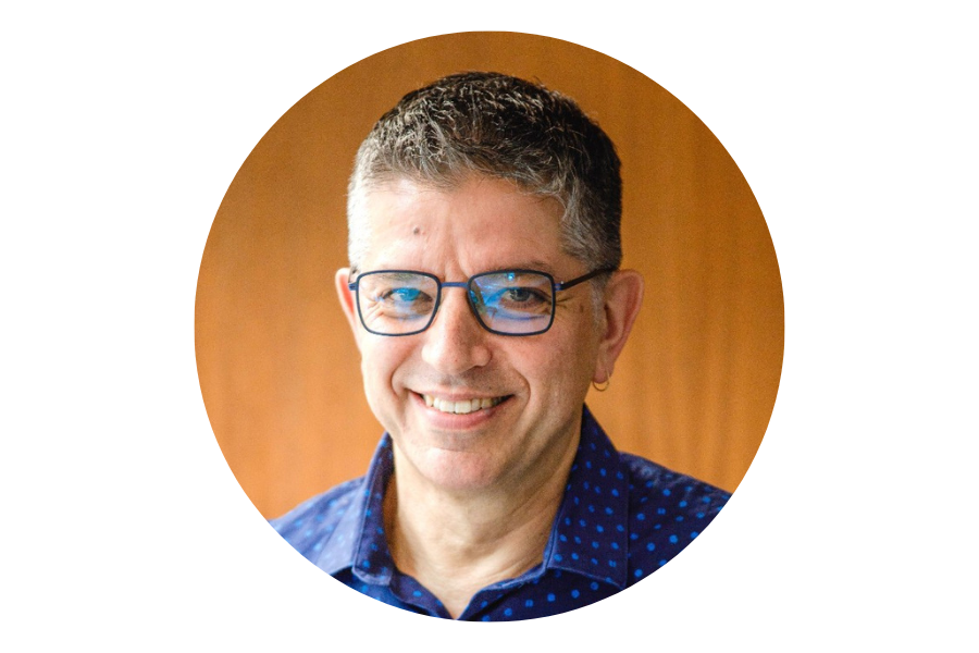 Photo of a man wearing a blue shirt and glasses with an orange wall in the background