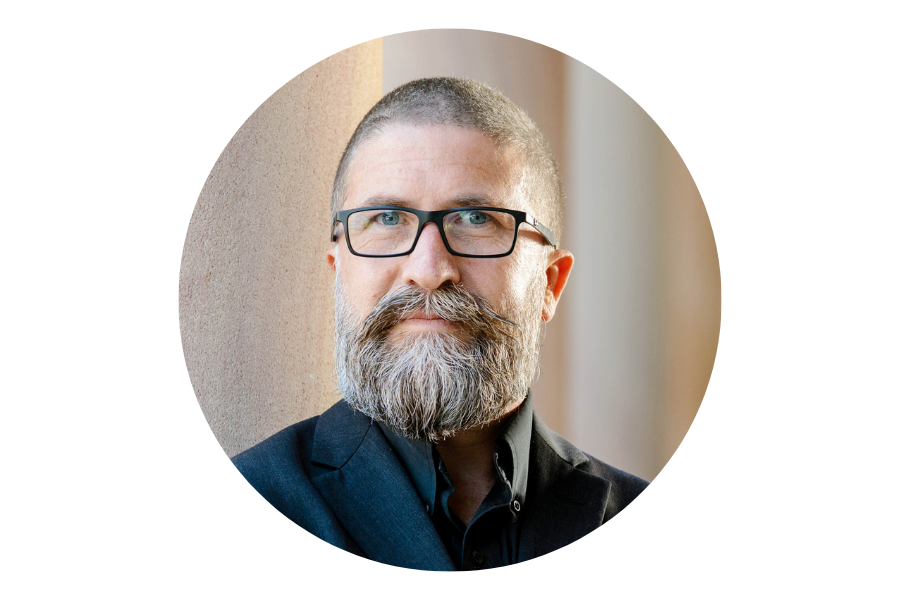 Photo of a man in a black jacket with glasses, leaning on a railing