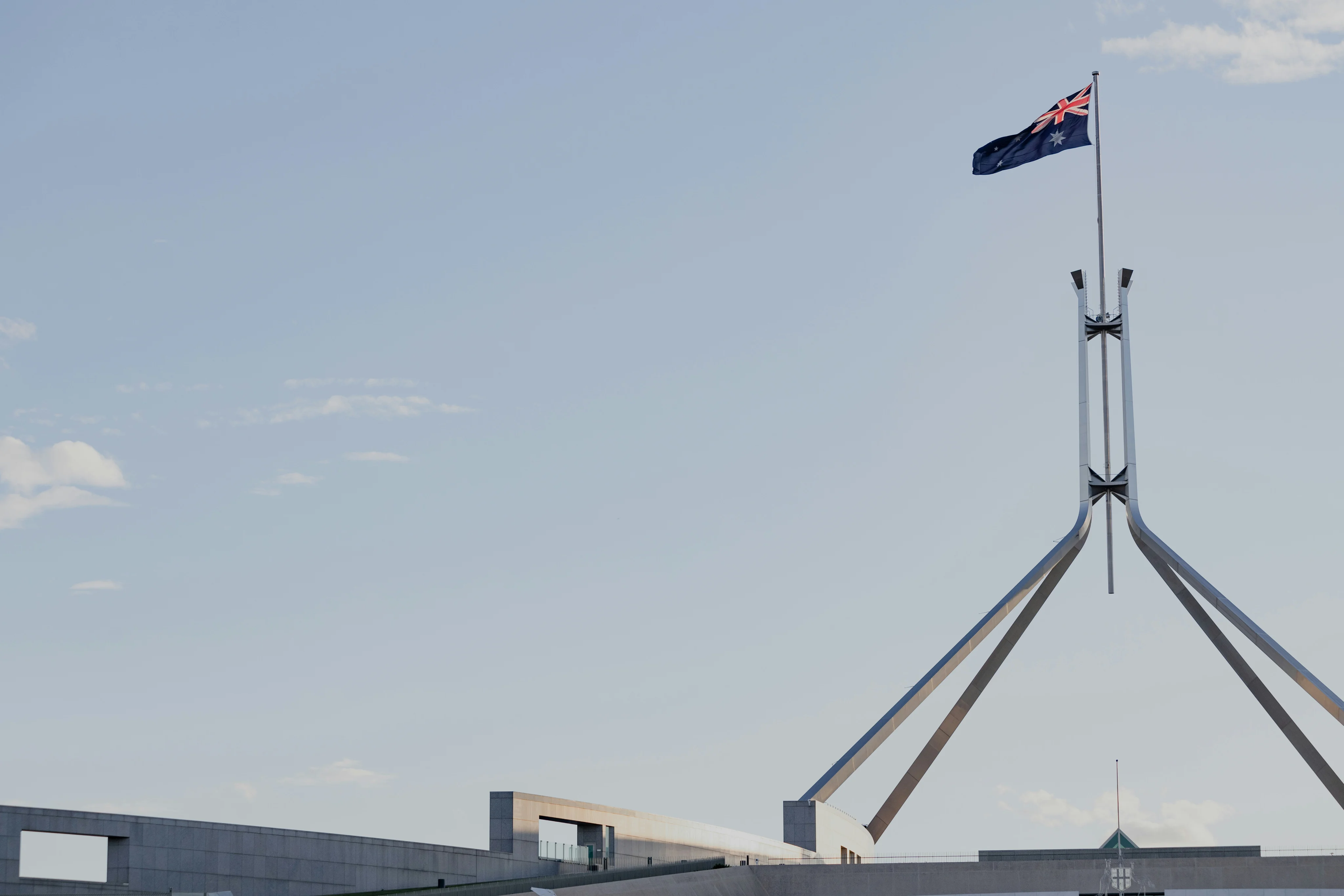 The Australian flag is pictured flying in the wind on a cloudless day. It sits on top of the spire at Parliament House in Canberra.