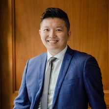 Professor Ryan Ko wearing a blue suit with a wooden panel background