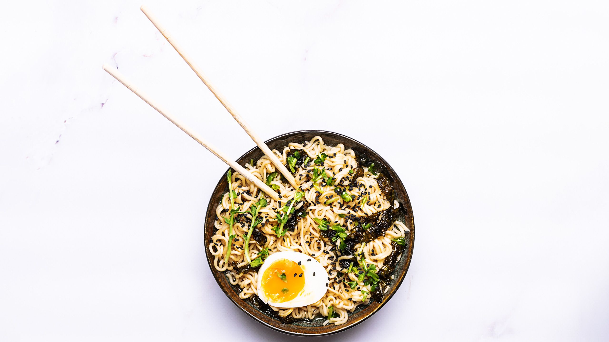 Ramen noodles with egg, shrimps, greens, seasame, seaweed and spices on white marble table close up. Traditional Asian soup