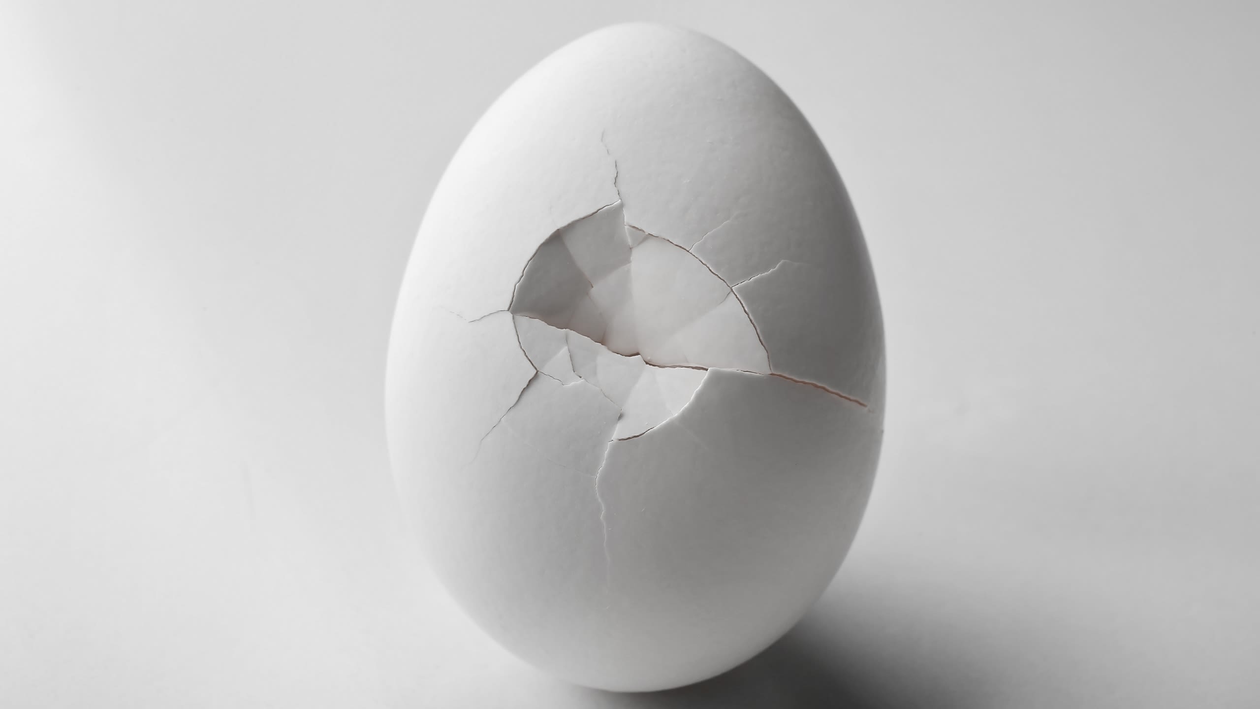 A cracked white egg on a white background.