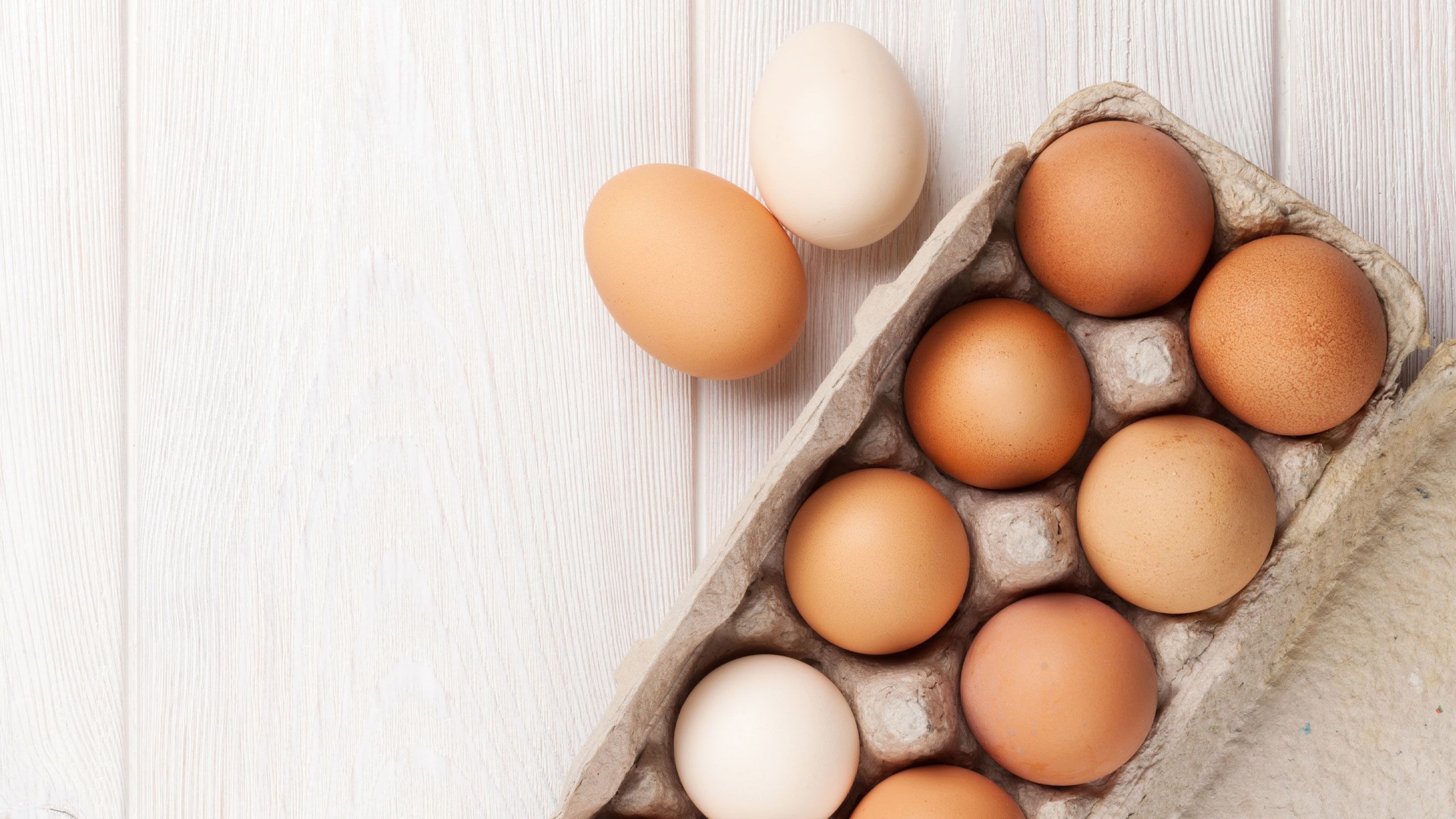 Cardboard egg carton filled with brown and white eggs on white wooden table top