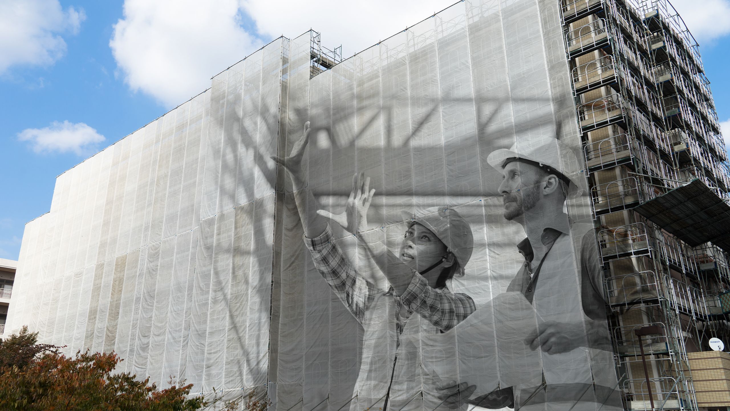 Young woman and man in hard hats and high-vis vests inspecting apartment construction site and holding building plans.