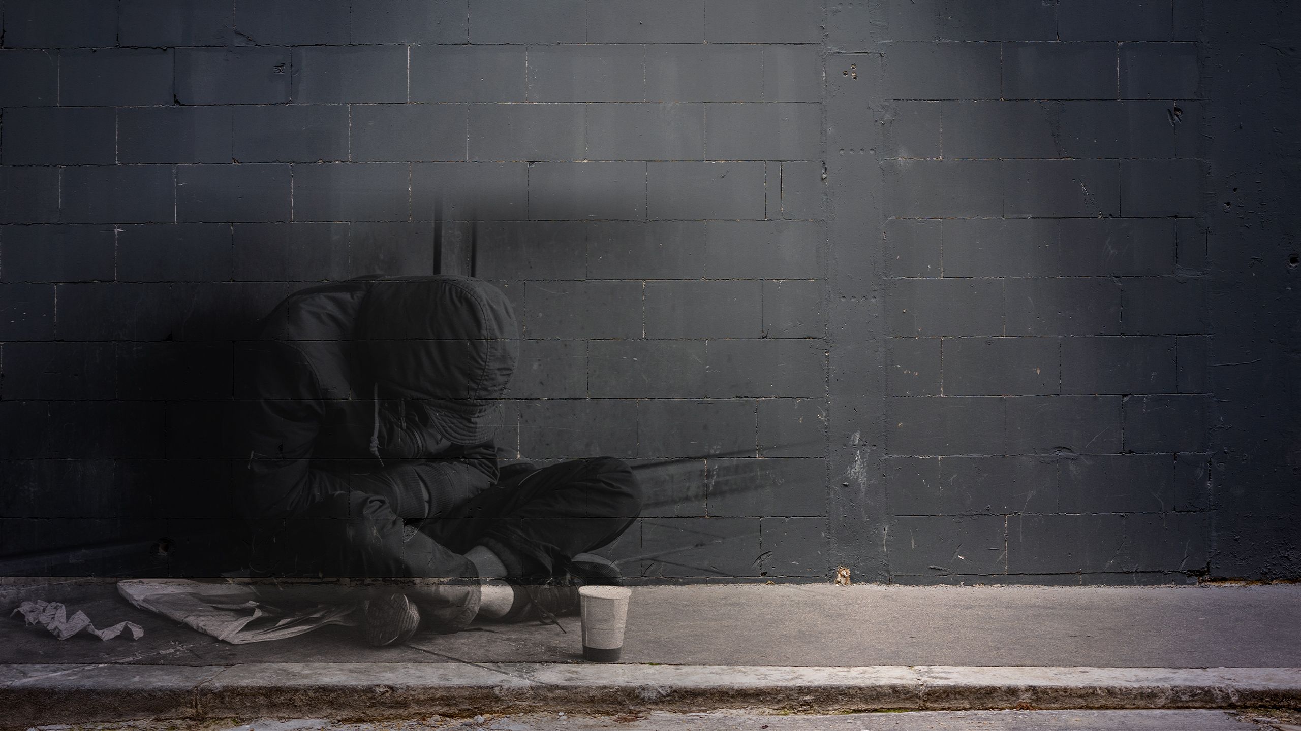 Homeless adult man sitting on the street in the shadow of the building.