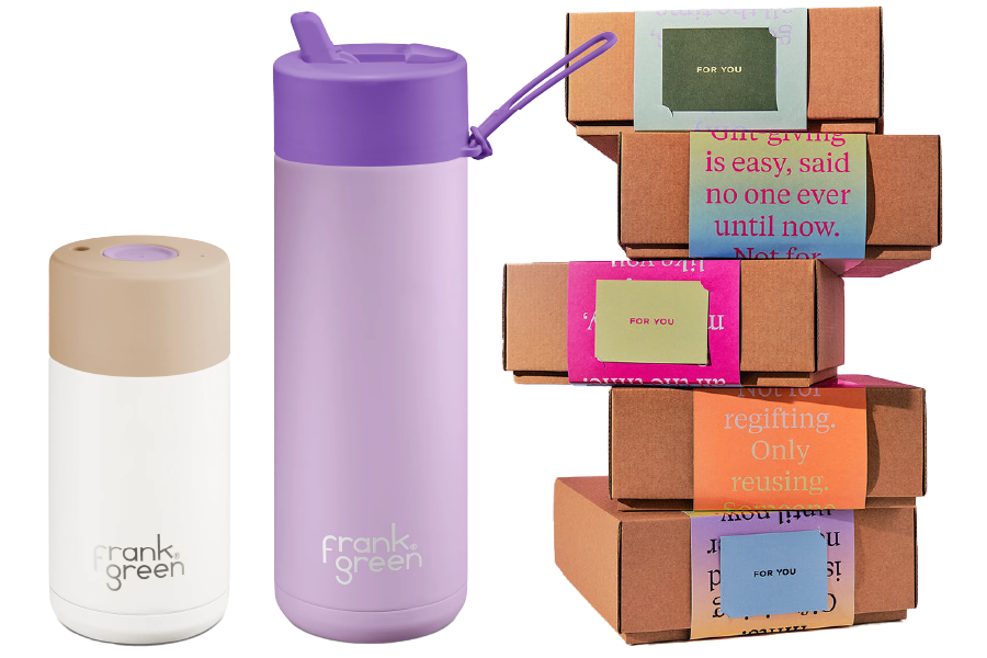 A Frank Green coffee cup in white and soft stone and a Frank Green water bottle in purple in front of a stack of Frank Green gift boxes