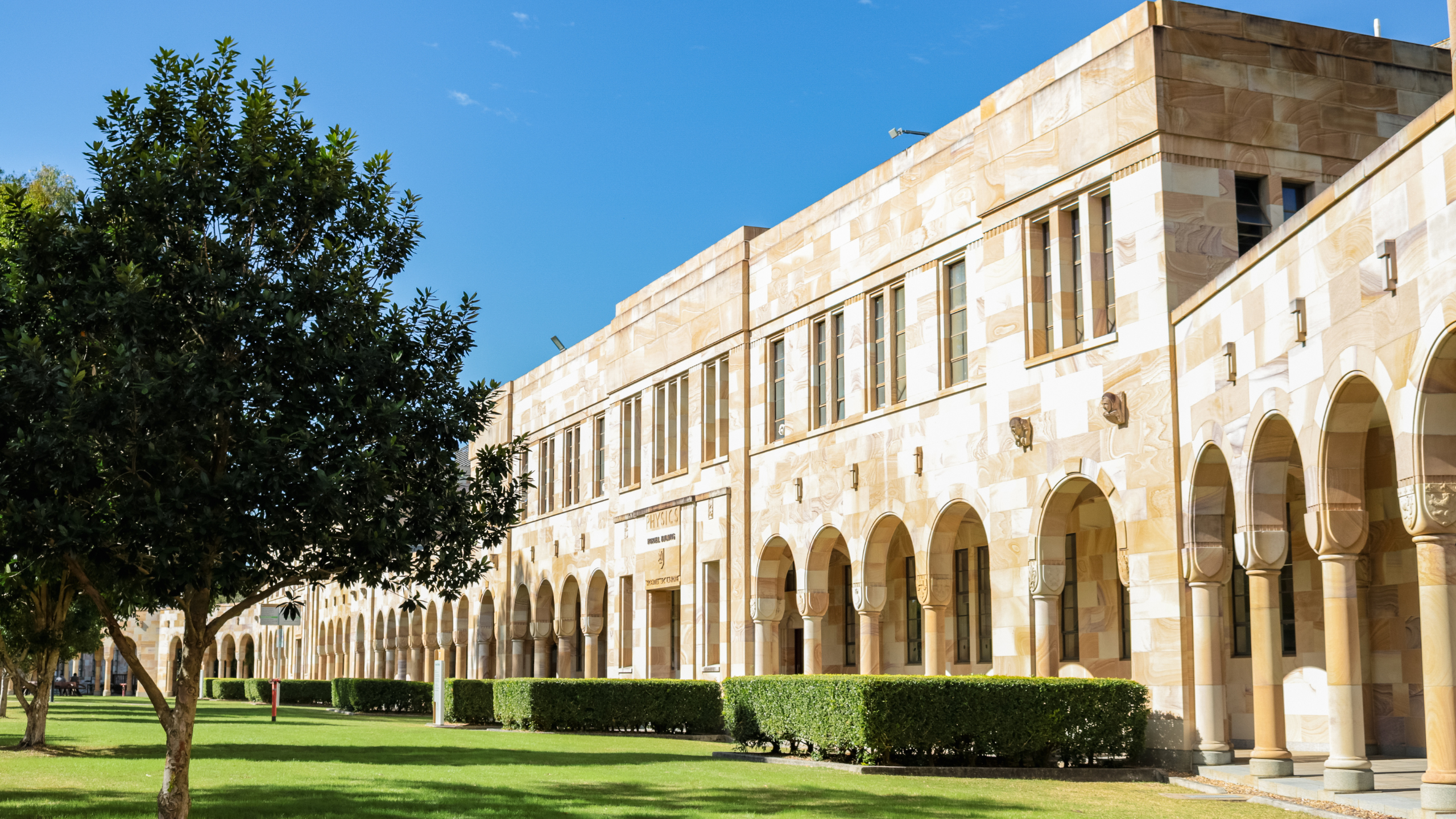 The Great Court sandstone buildings are featured against the grass on a sunny day.