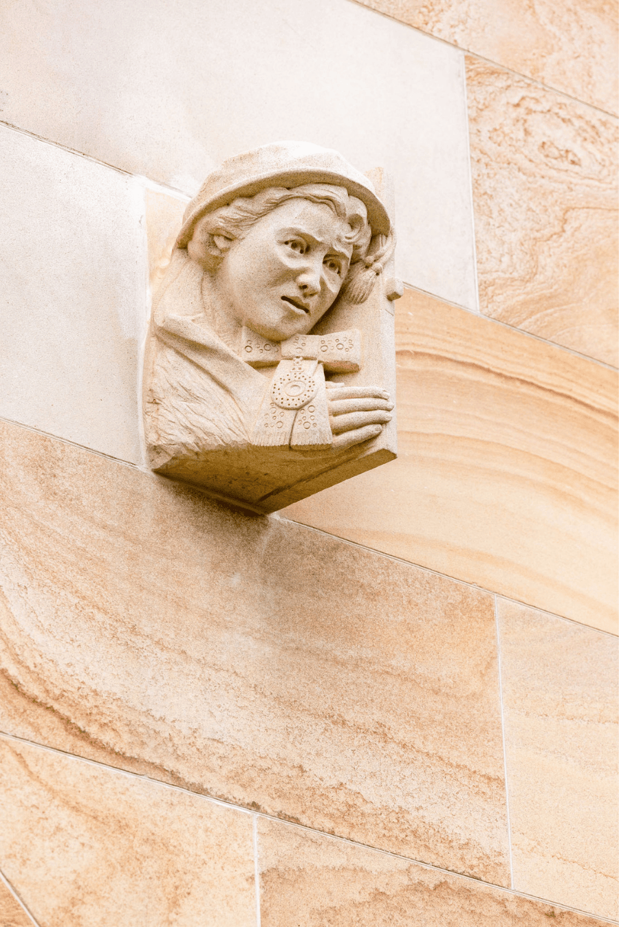 A close up of the final grotesque. Valadian is carved in sandstone in her academic gown and bonnet, pushing open a door.