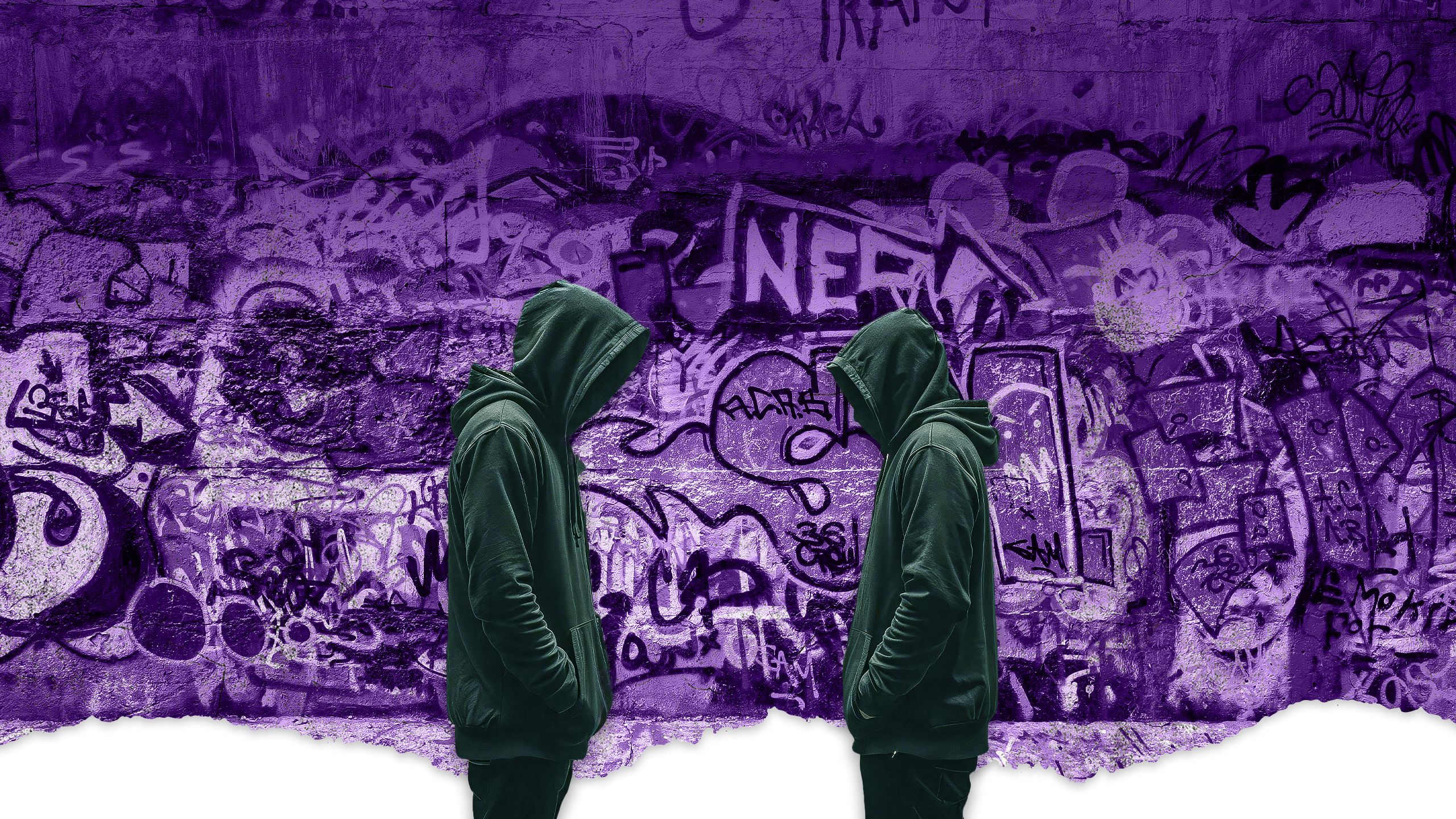 An image of two youths in black hooded jumpers standing in front of a wall covered in graffiti.