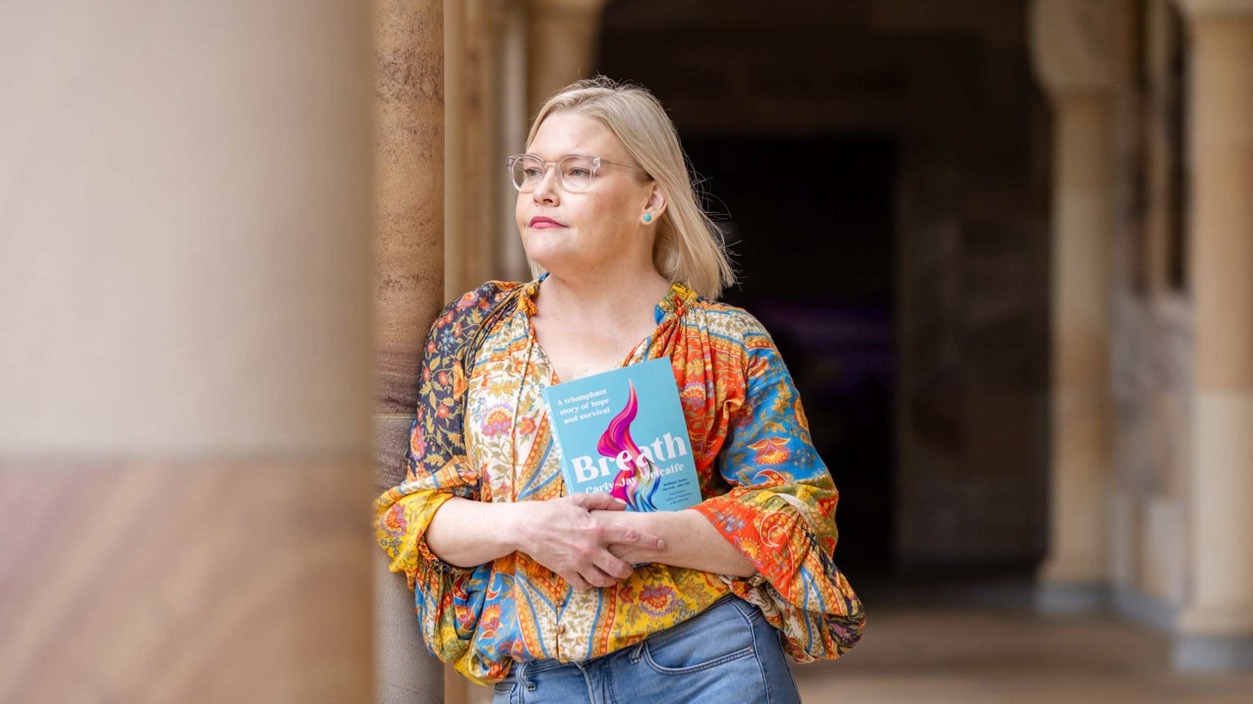 An image of Carly-Jay Metcalfe standing in UQ's Great Court with her new book, Breath.