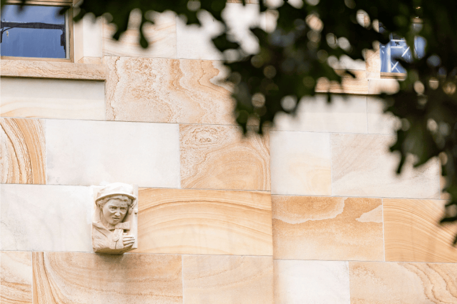 The final grotesque of Margaret Valadian is now in its final place in the Great Court. It sits against a backdrop of sandstone walls and greenery.