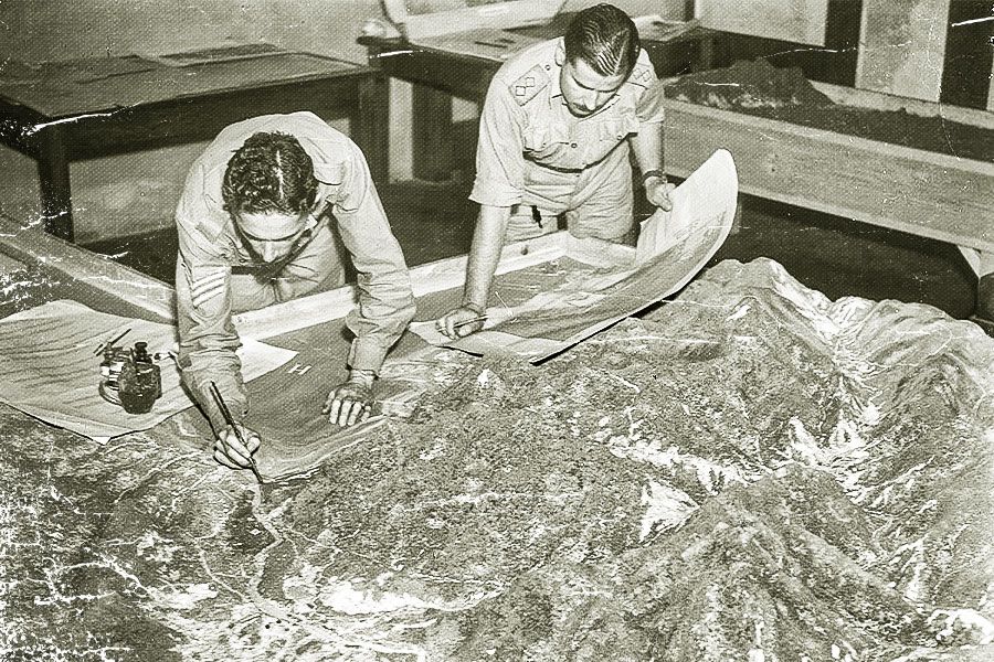 Sergeant M. R. Angus (left) and AND Lieutenant J. E. Maher of General Staff Intelligence, Advanced Land Headquarters working on a model of the New Guinea area inside the (now) Forgan Smith building.