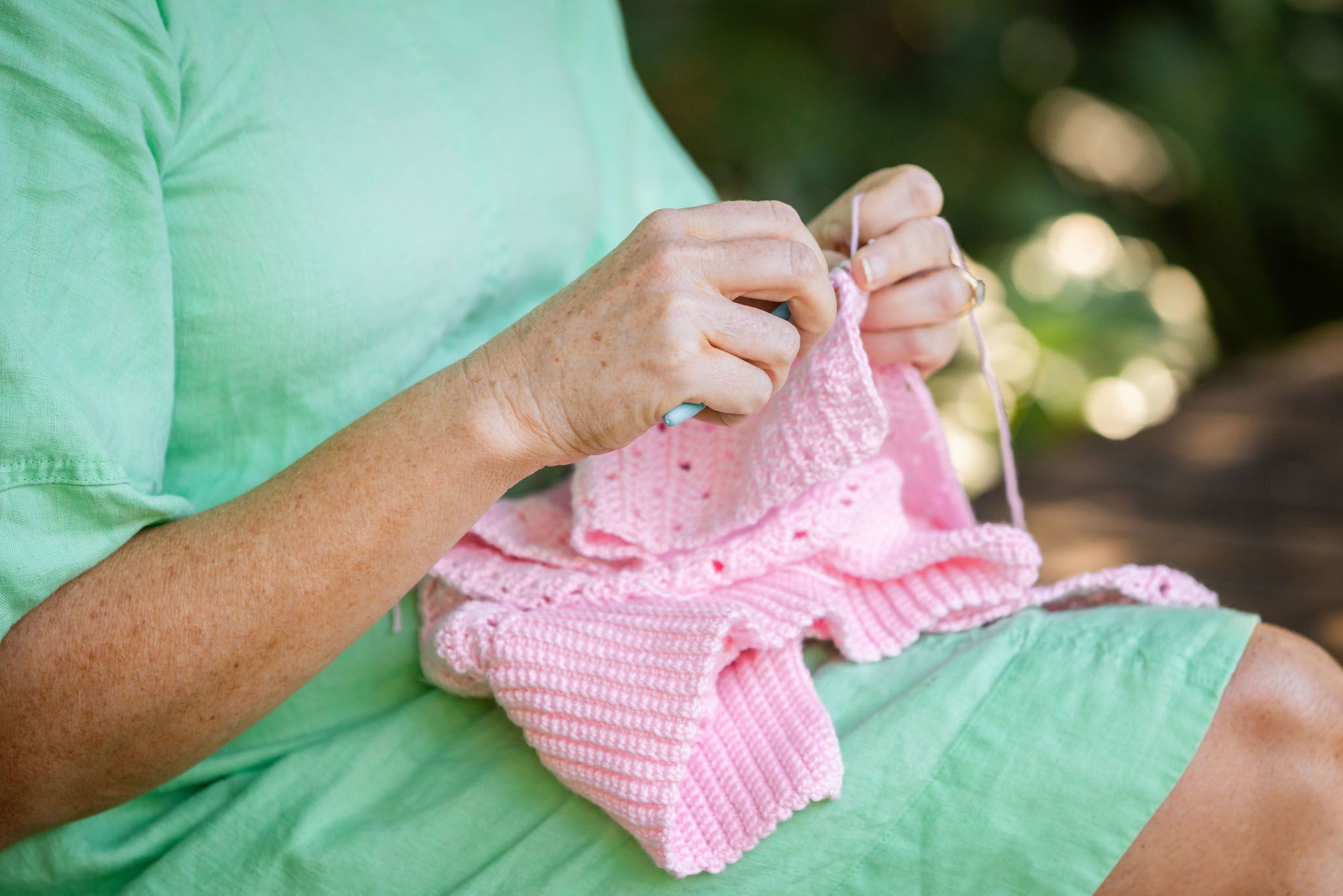 Two hands work on a pink crocheted sweater