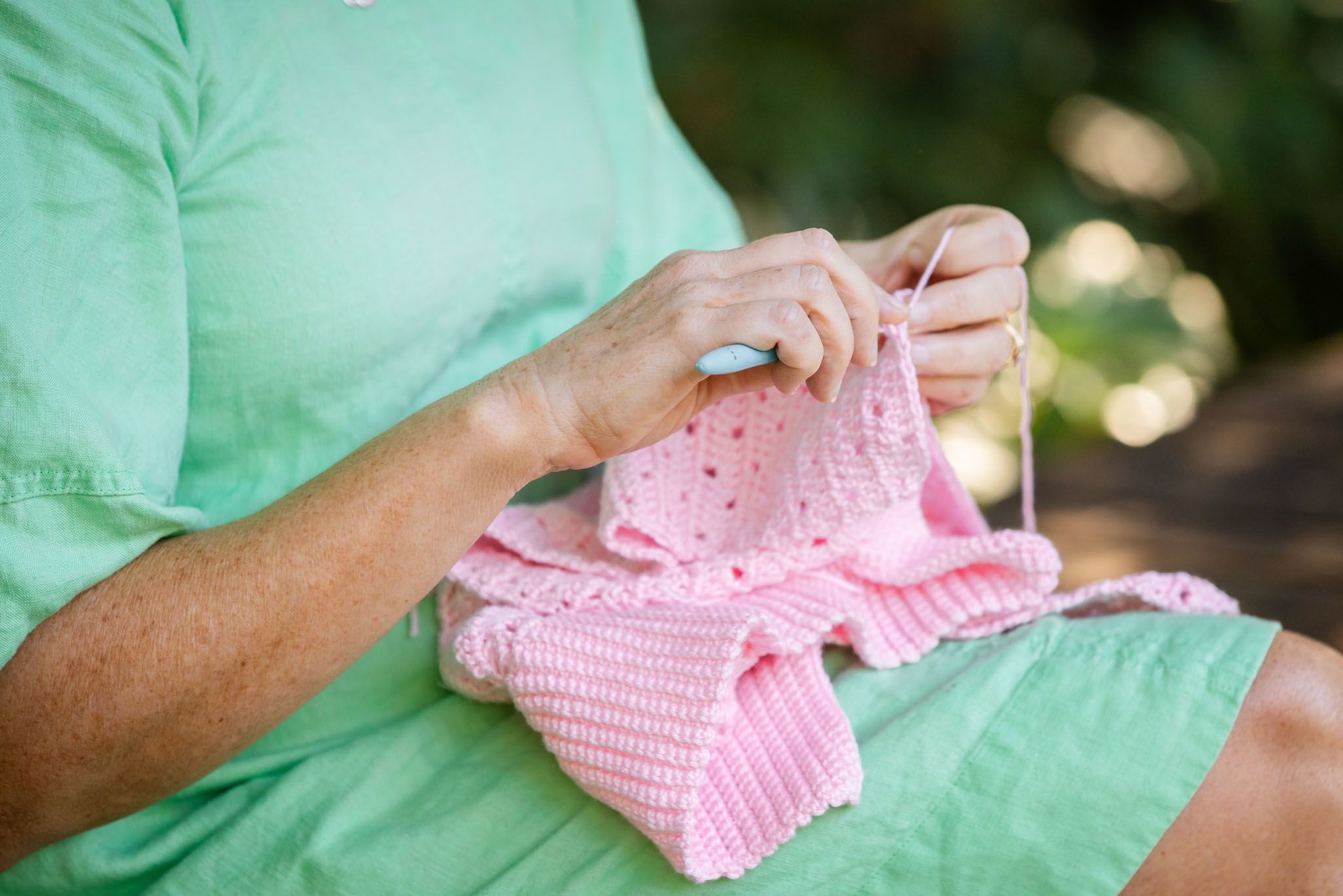 Two hands work on a pink crocheted sweater