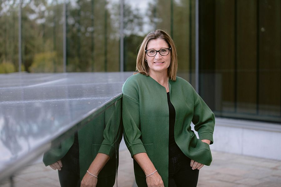 Professor Lorraine Mazerolle smiling in front of a glass building and reflective rectangular statue