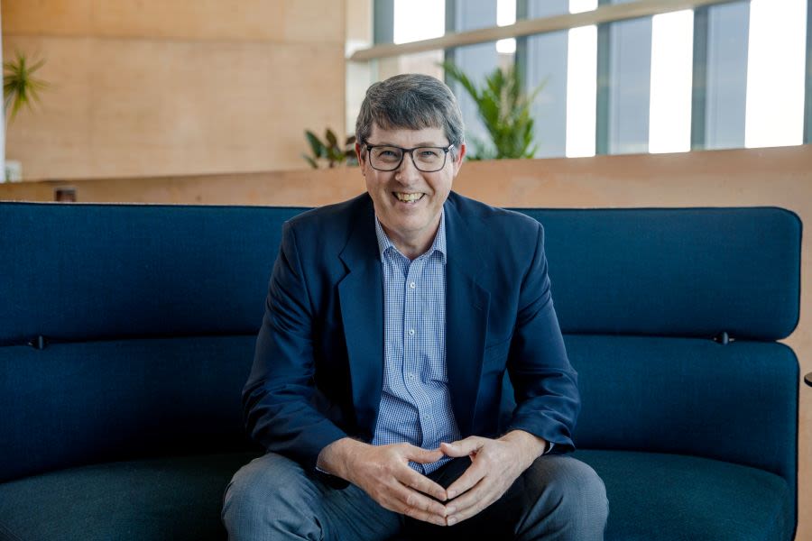 Professor Bruce Abernethy smiling broadly sitting on a lounge chair and smiling