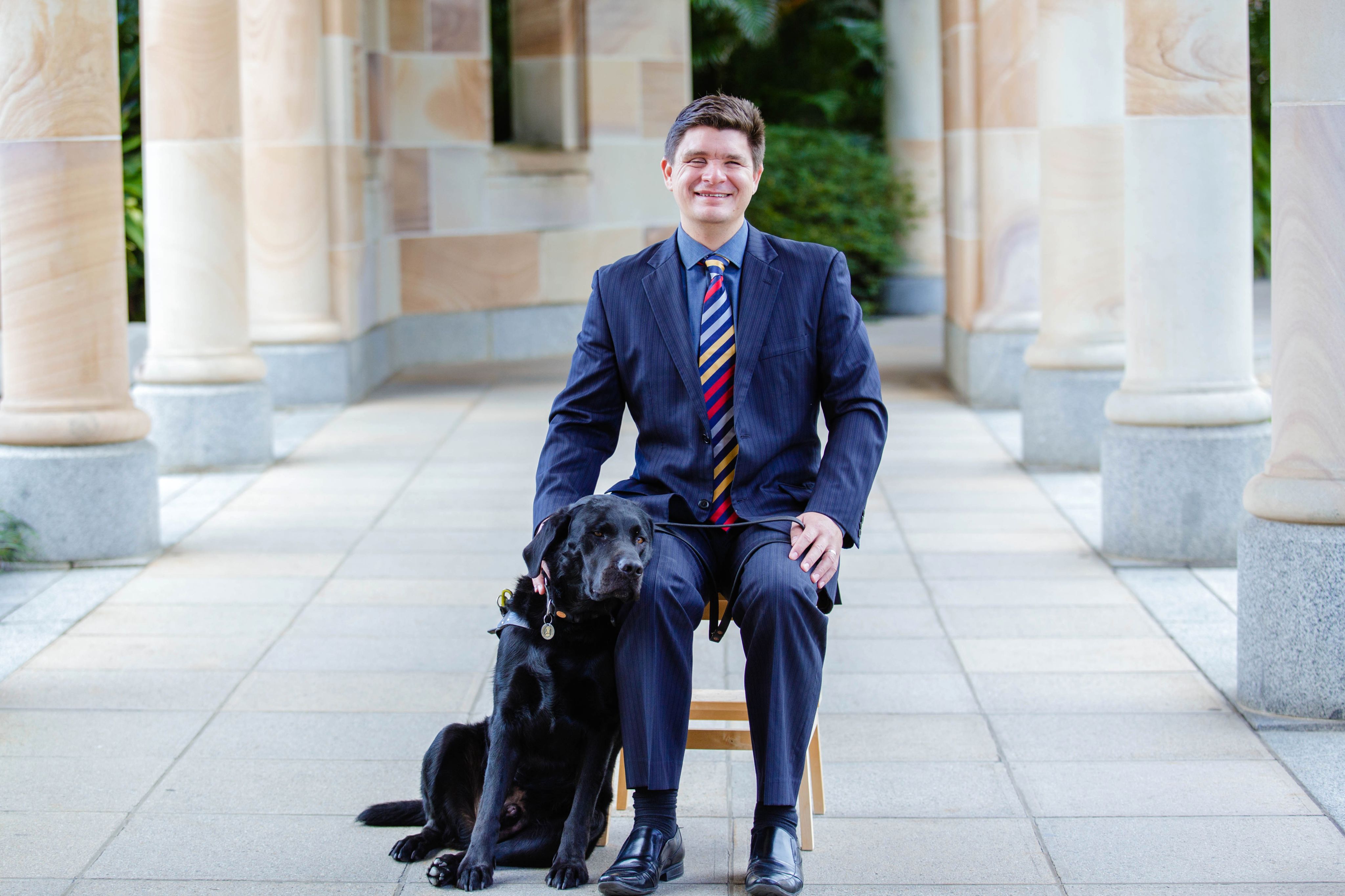 Professor Paul Harpur and his guide dog in a walkway lined with sandstone columns