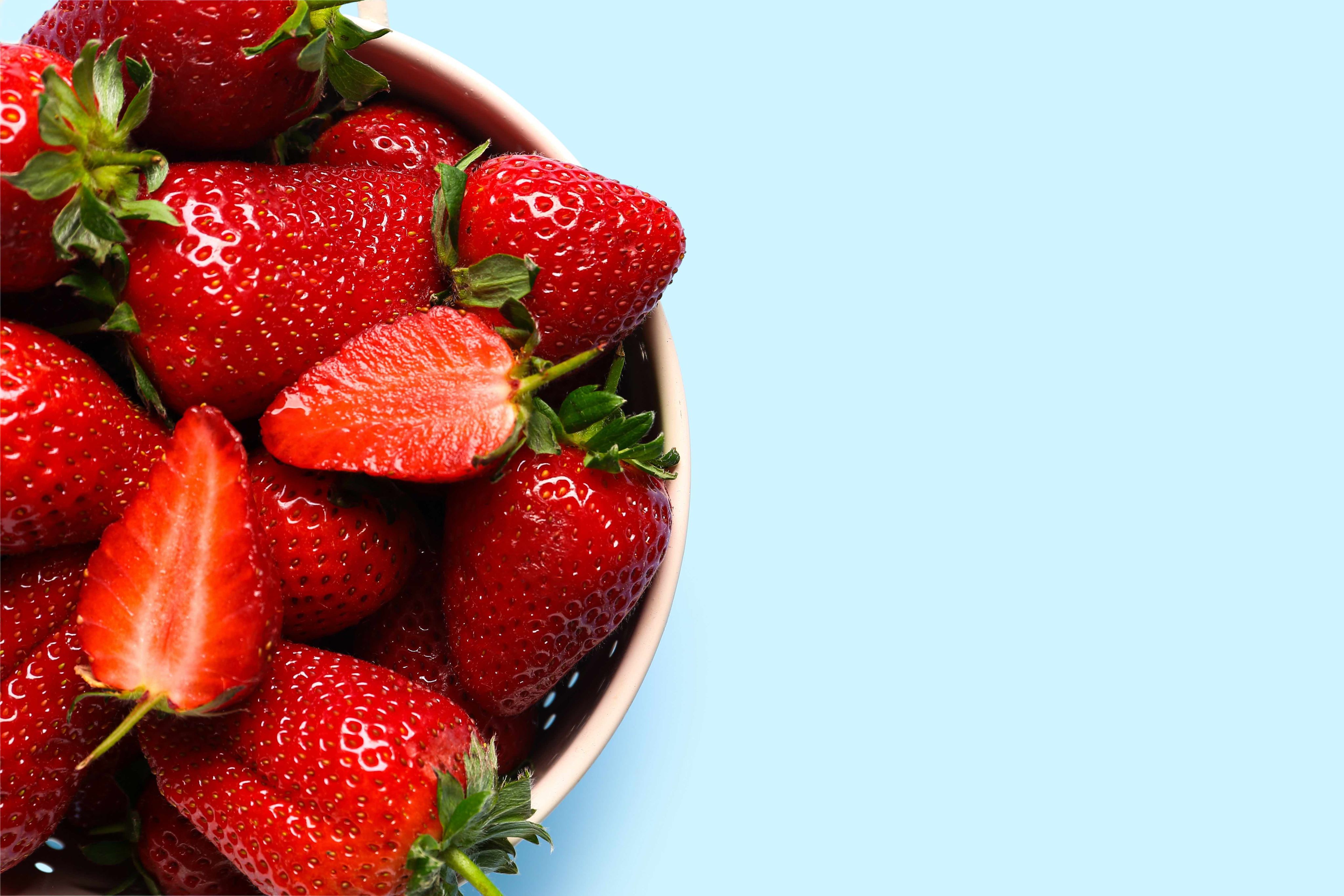 A flat lay image of strawberries in a colander on a light blue background