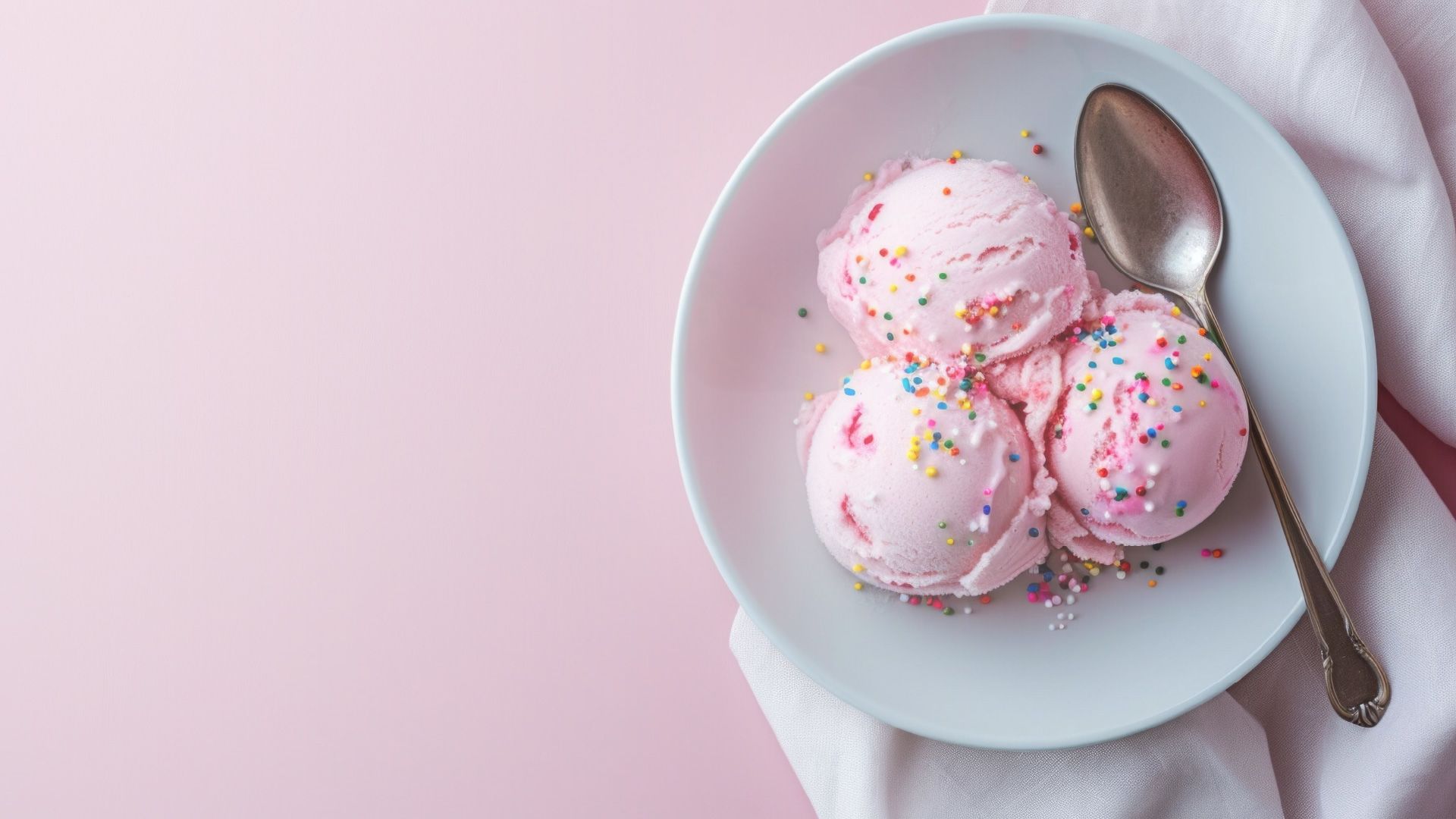 A flat lay image of a bowl of pink ice cream with sprinkles on a pink background