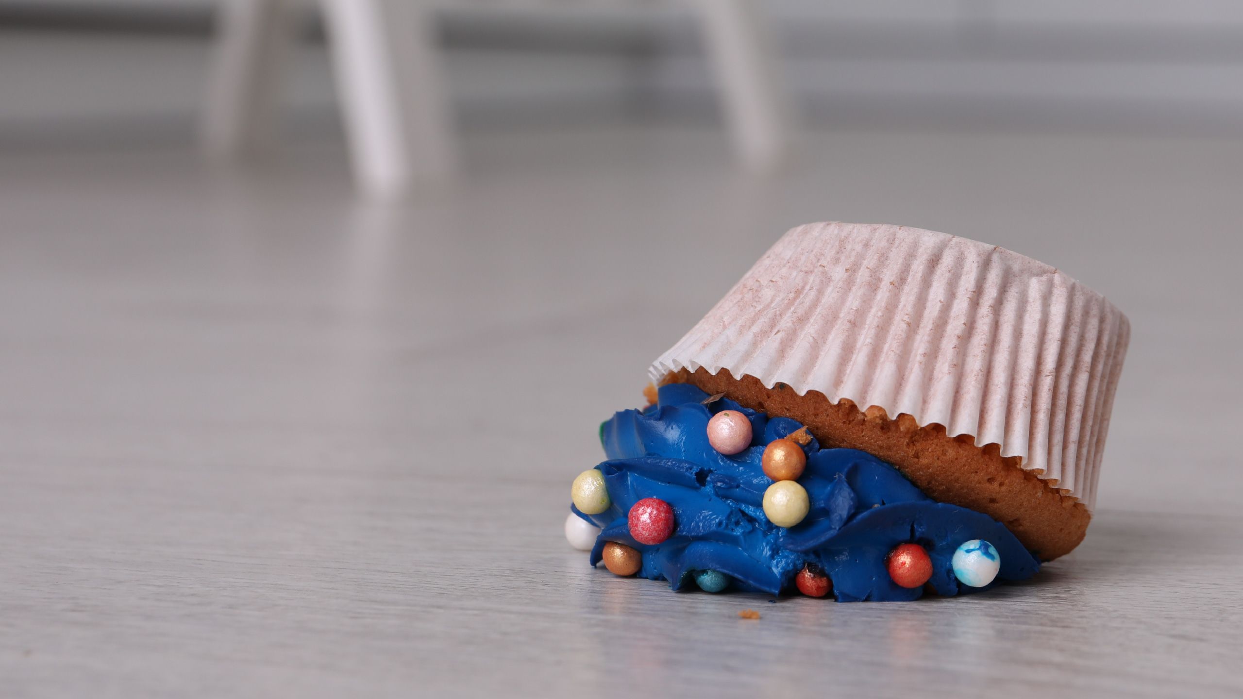 A cupcake with blue icing is lying upside down on the floor after being dropped