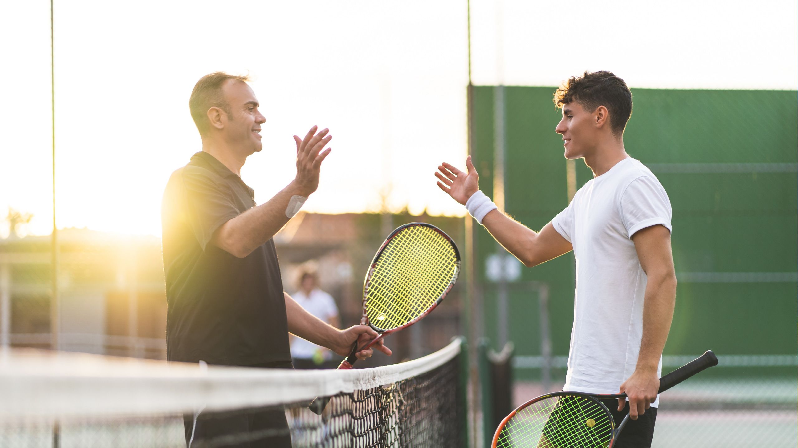 Two male tennis players go to shake hands at the net.