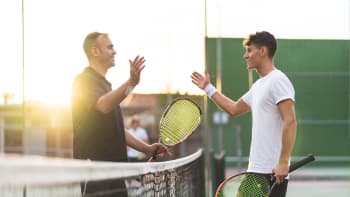 Two male tennis players go to shake hands at the net.