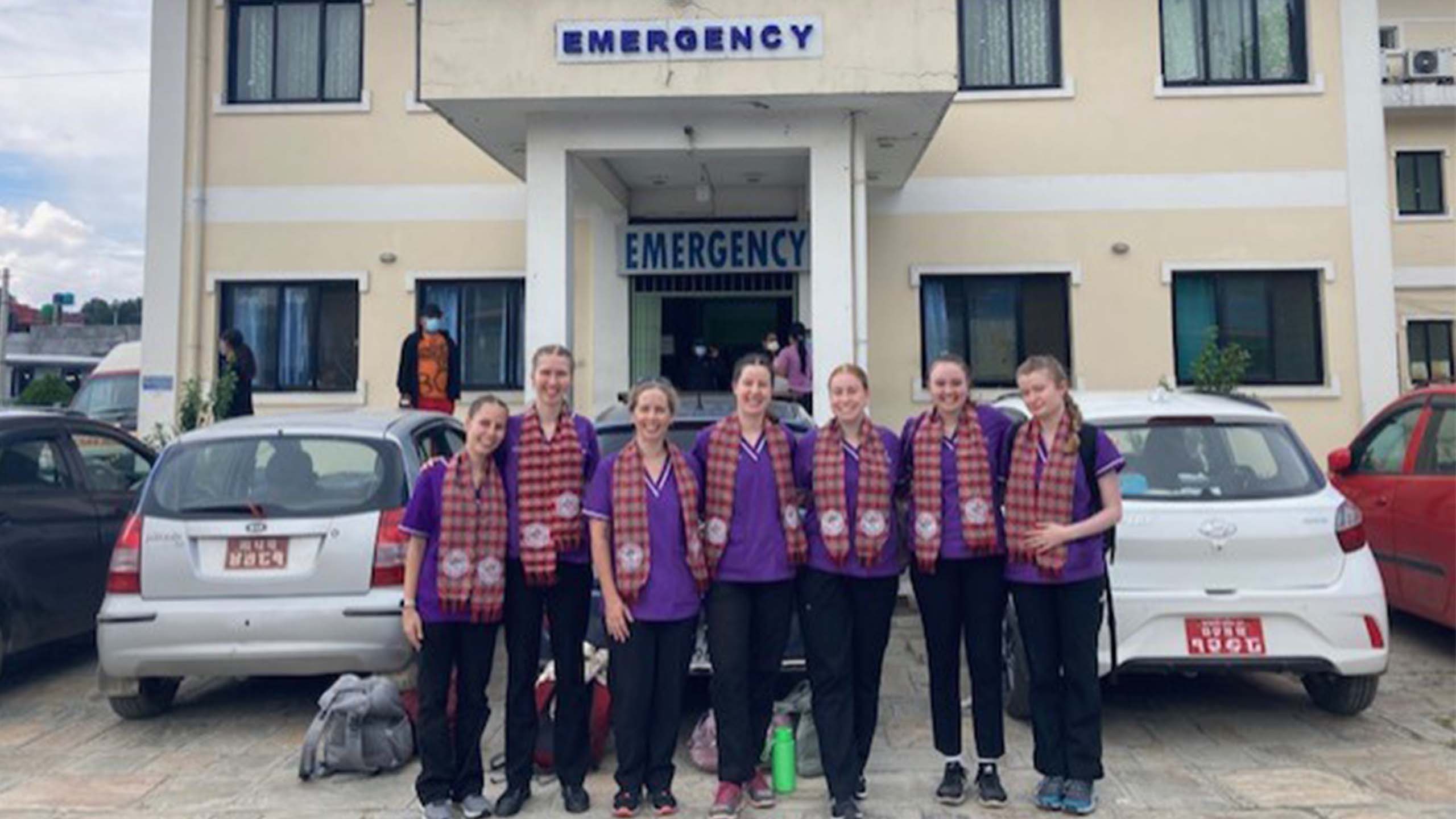Nine UQ students stand in a line for a group photo. They are all wearing purple UQ scrub tops and red/white check pattern