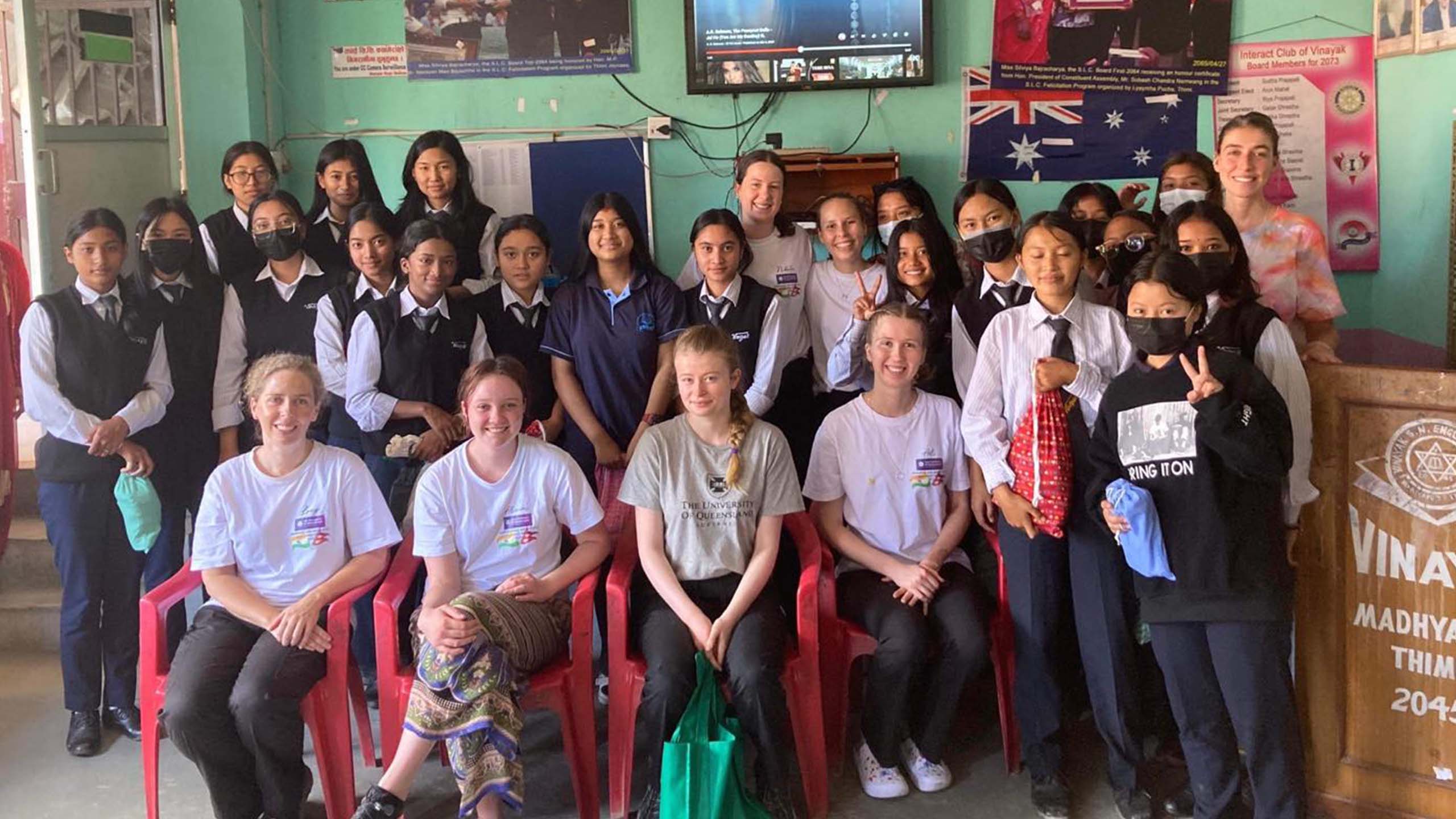 UQ students sitting on chairs while a class of Nepalese schoolgirls stand behind them for a group photo.