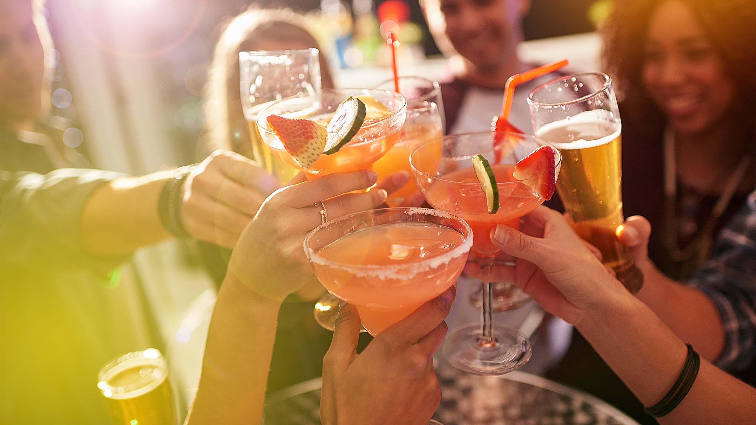 Group of people 'cheers-ing' various alcoholic beverages including beer and cocktails.
