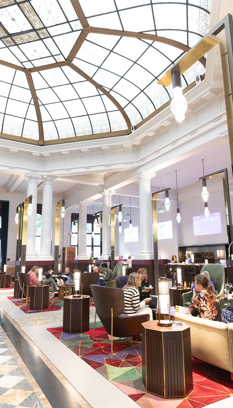 Image of a room with a high glass circular ceiling. The room has various couched in which attendees are sitting and chatting