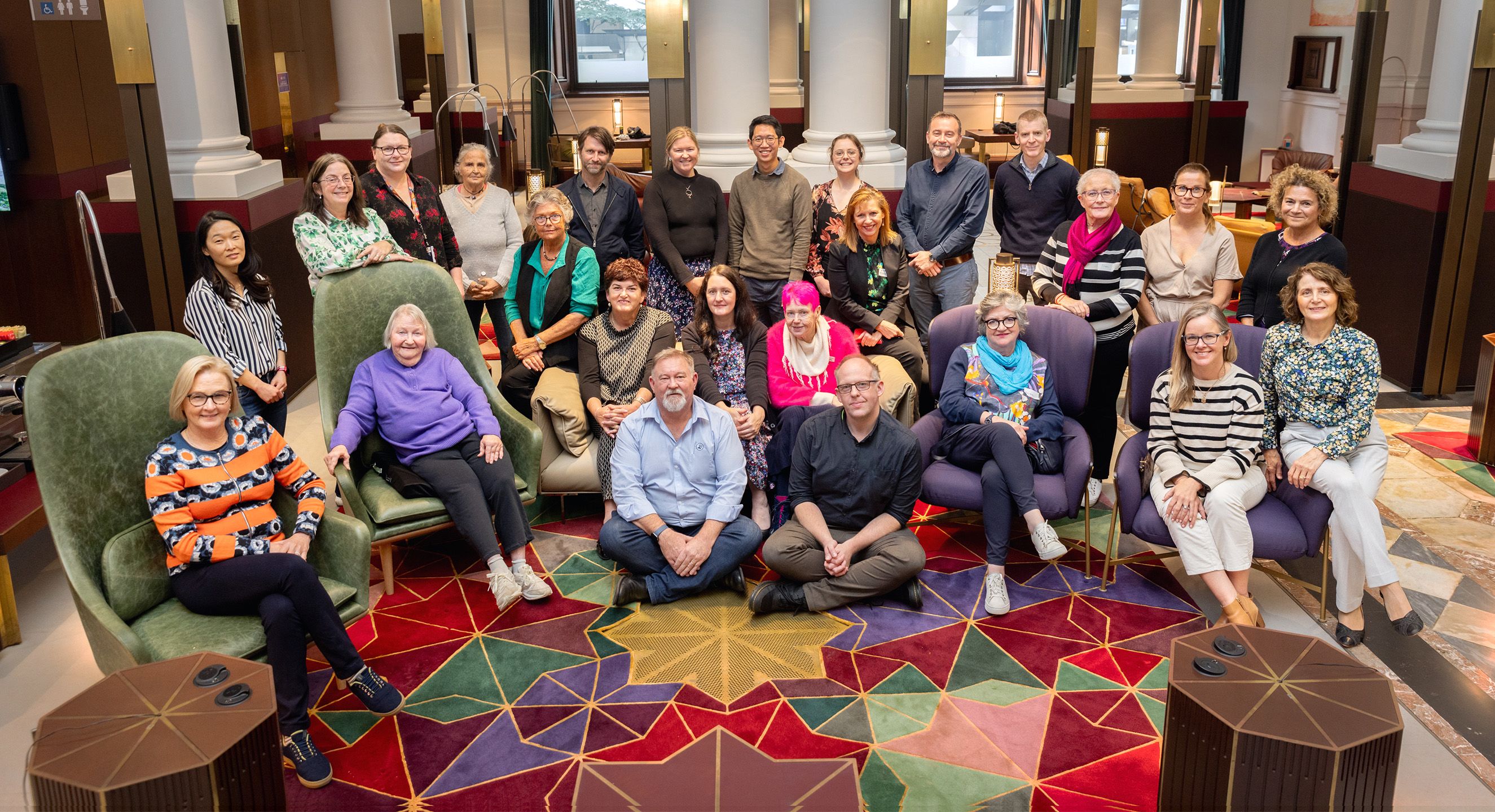 A group photo of 25 people. They are positioned in tiered rows smiling at the camera