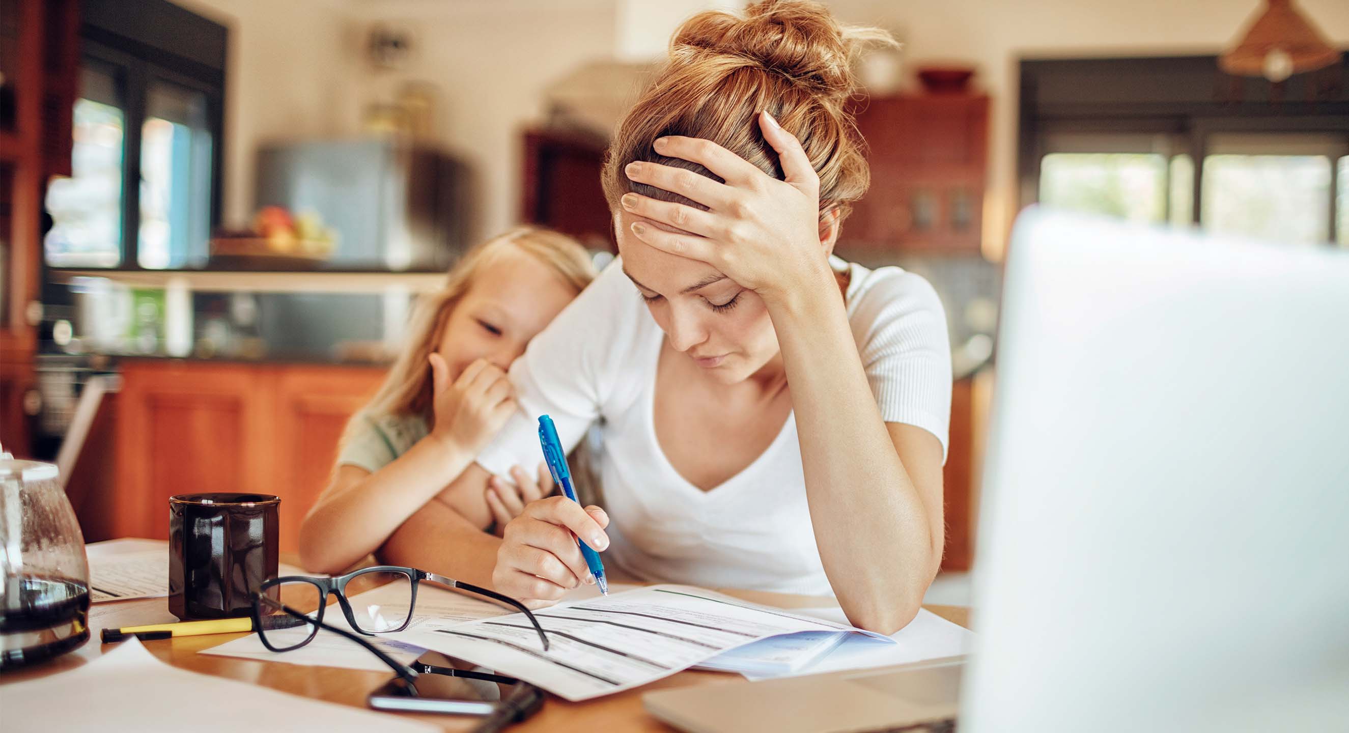 A woman hold her hand on her head in a stressed motion while filling in a form as her daughter holds her arm