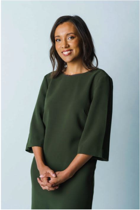 Isabella Higgins, a young woman wearing a forest green dress, smiling with her hands clasped in front of her