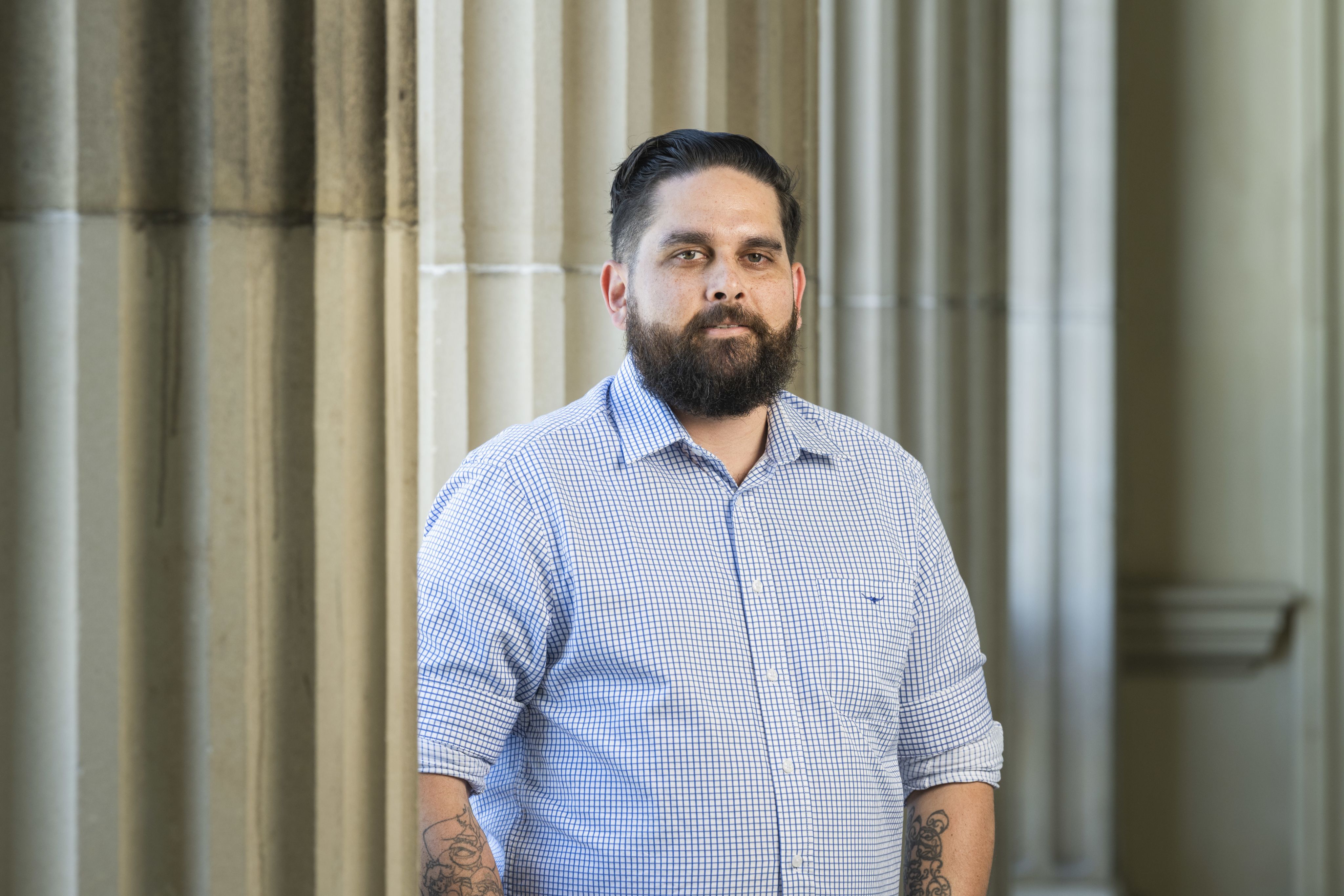 A headshot of Kieren Marr, a man with dark hair and a beard, wearing a blue checkered long-sleeved shirt