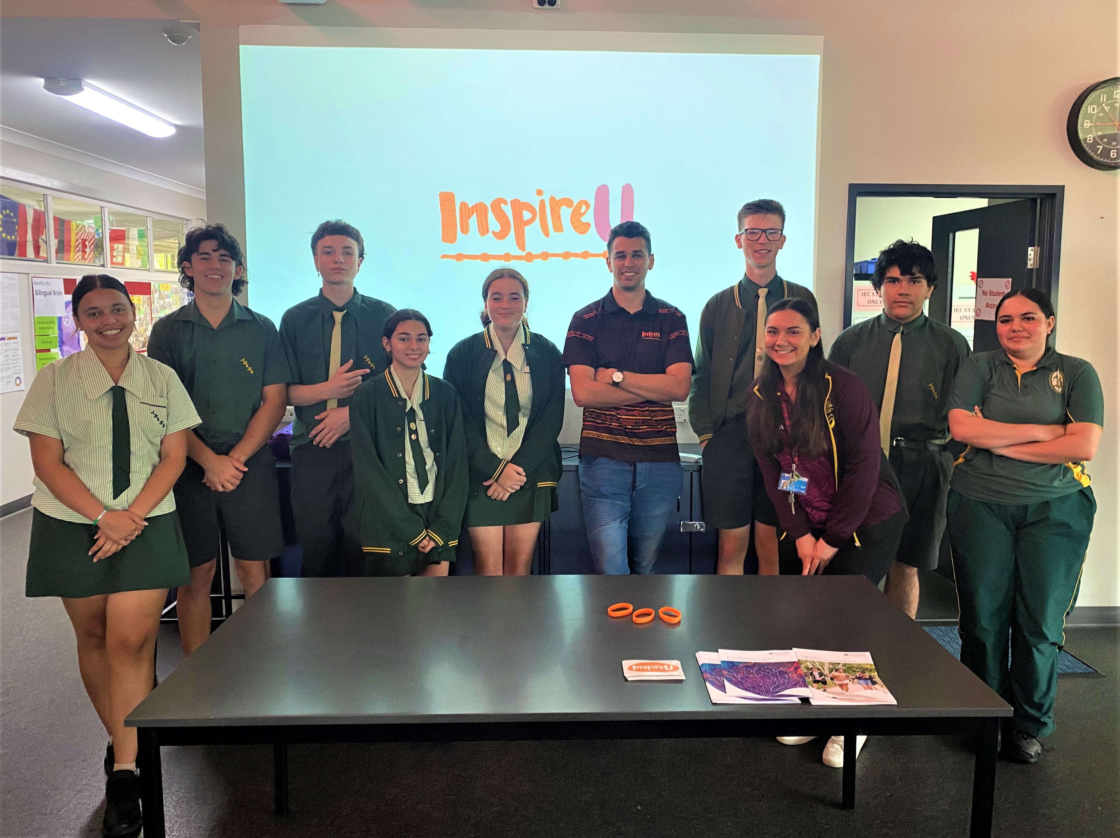 A group of high school students in their uniforms standing in front of a wall projection with the InspireU logo