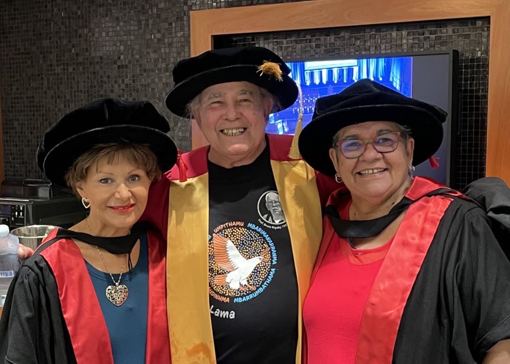Professor Bronwyn Fredericks, Dr Kev Carmody, and Professor Tracey Bunda huddled for a photo wearing academic robes