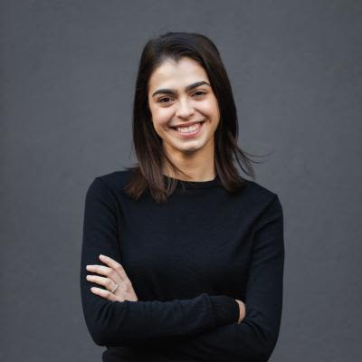 A headshot of Georgia Birks, a young woman wearing all black, smiling widely with her arms crossed.