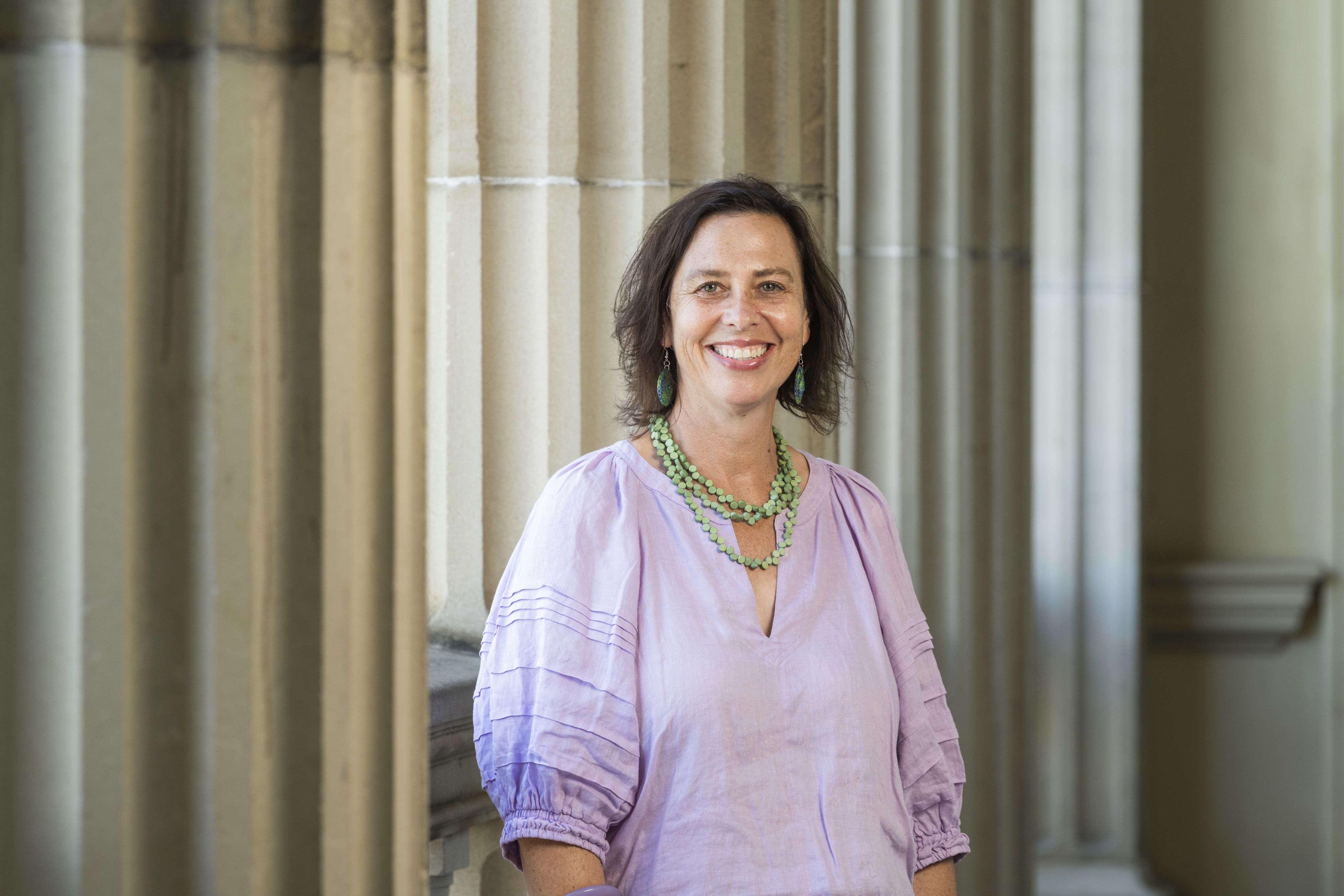 A headshot of Megan Gaynor, a woman with short dark hair wearing a lilac shirt and green necklace