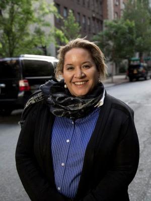 Megan Davis, a woman with light brown hair, standing on a city street in front of brown brick buildings and smiling